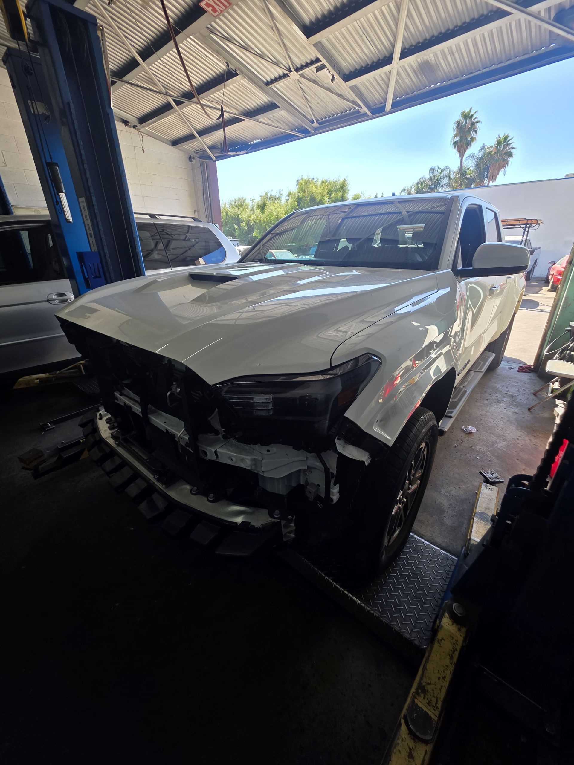 Damaged white pickup truck with front-end collision damage in a garage bay