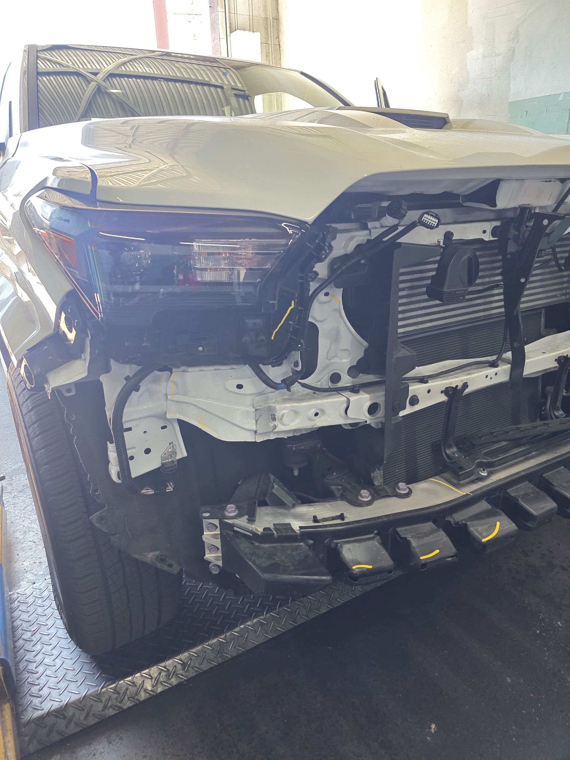 Front view of a damaged black SUV with missing bumper and exposed grille in a garage