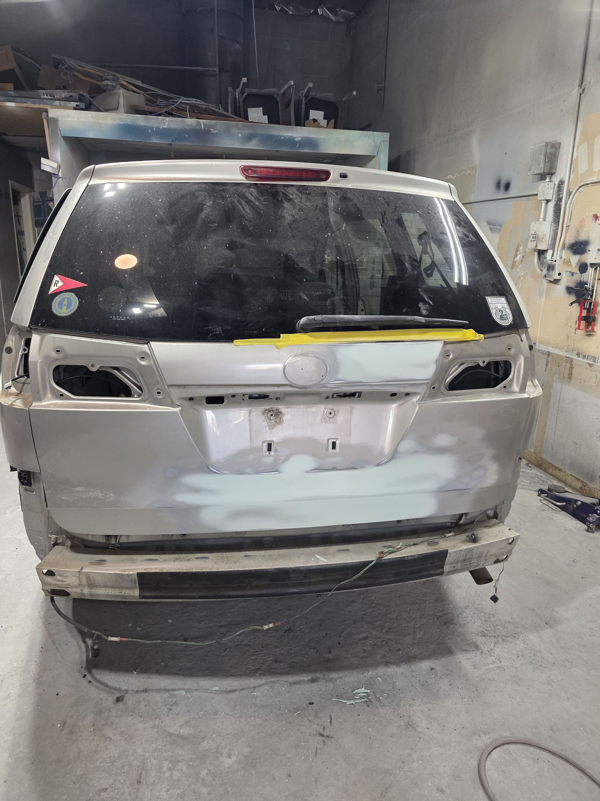 Damaged white SUV rear in an auto body shop, with taped-off taillights and dented bumper area