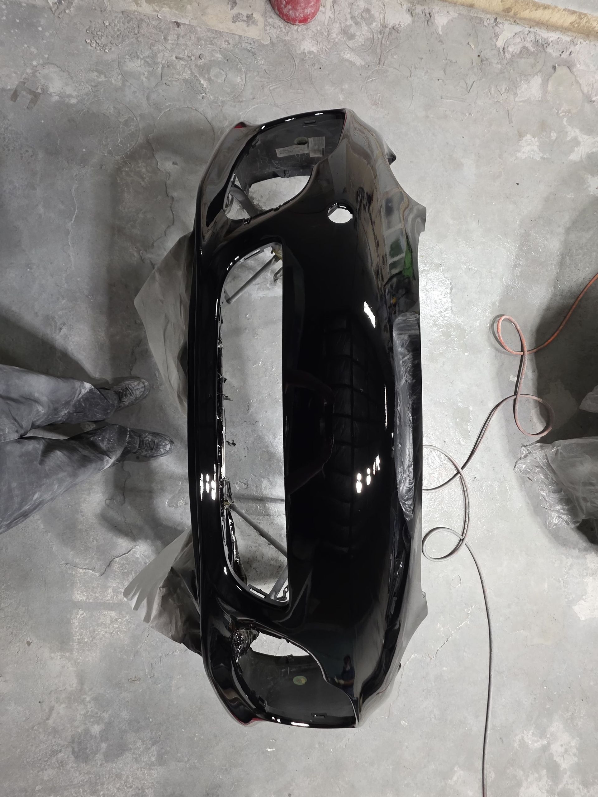 Black car body shell viewed from above on a concrete floor, with wires and debris around it