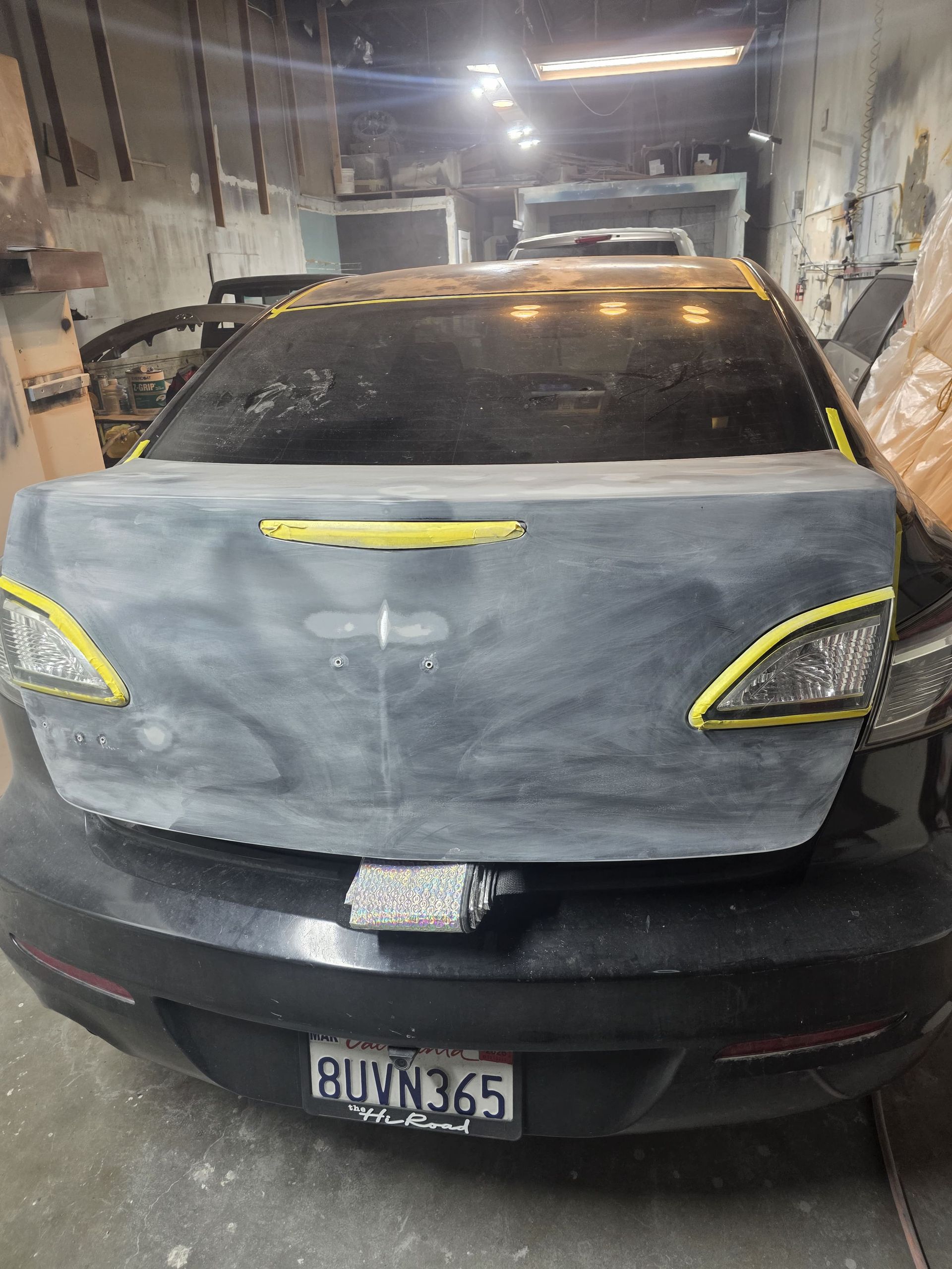 Damaged black car with taped headlights parked in a garage, front bumper missing.