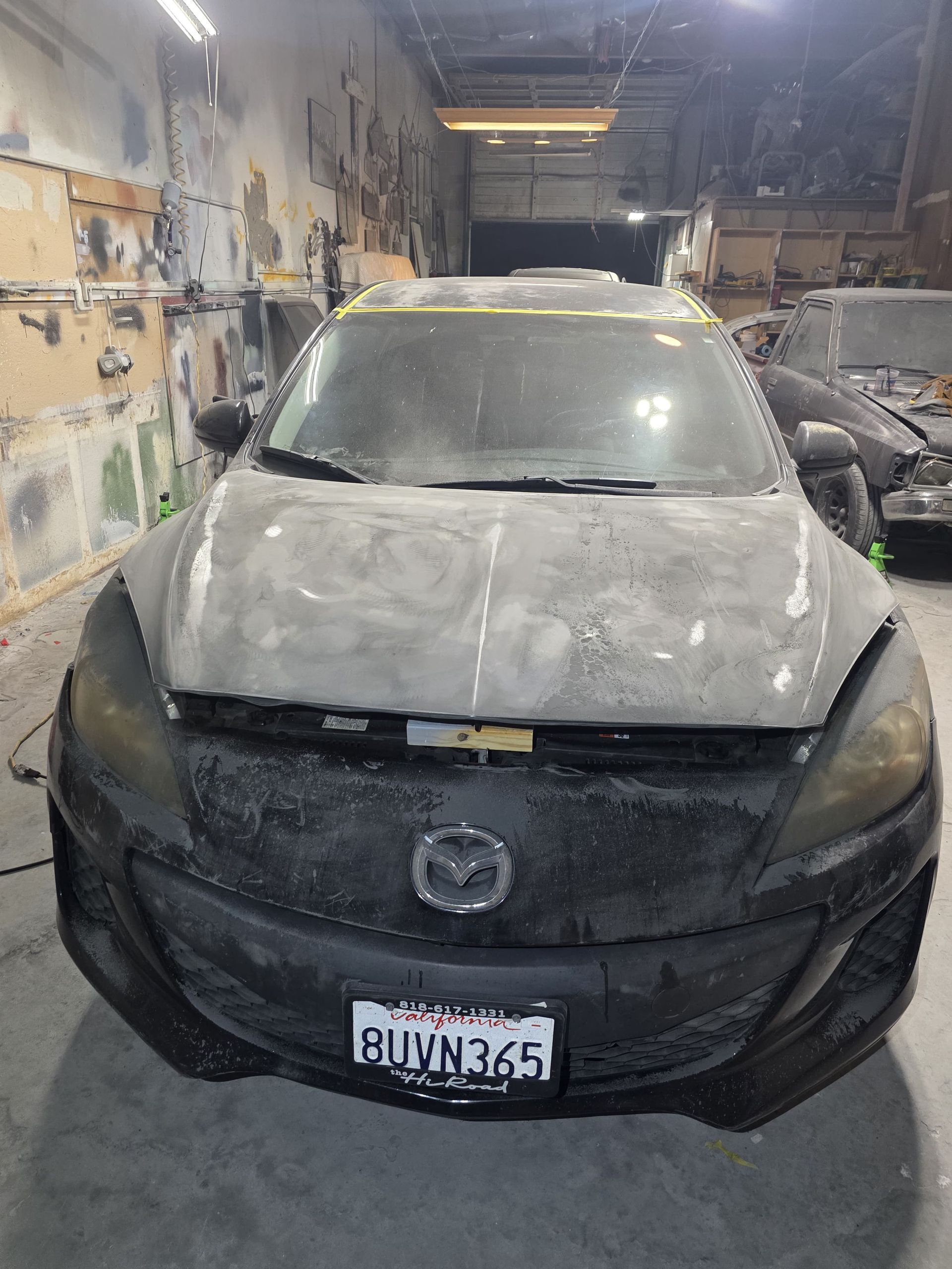 Dust-covered black car parked inside a dirty garage, front view, with a Chevrolet emblem on the grille