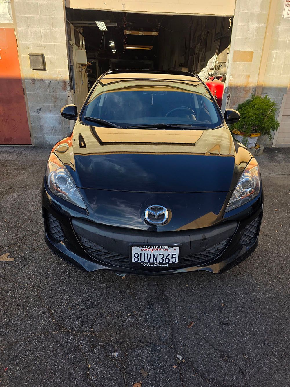 Black Mazda parked in front of an open garage on a driveway