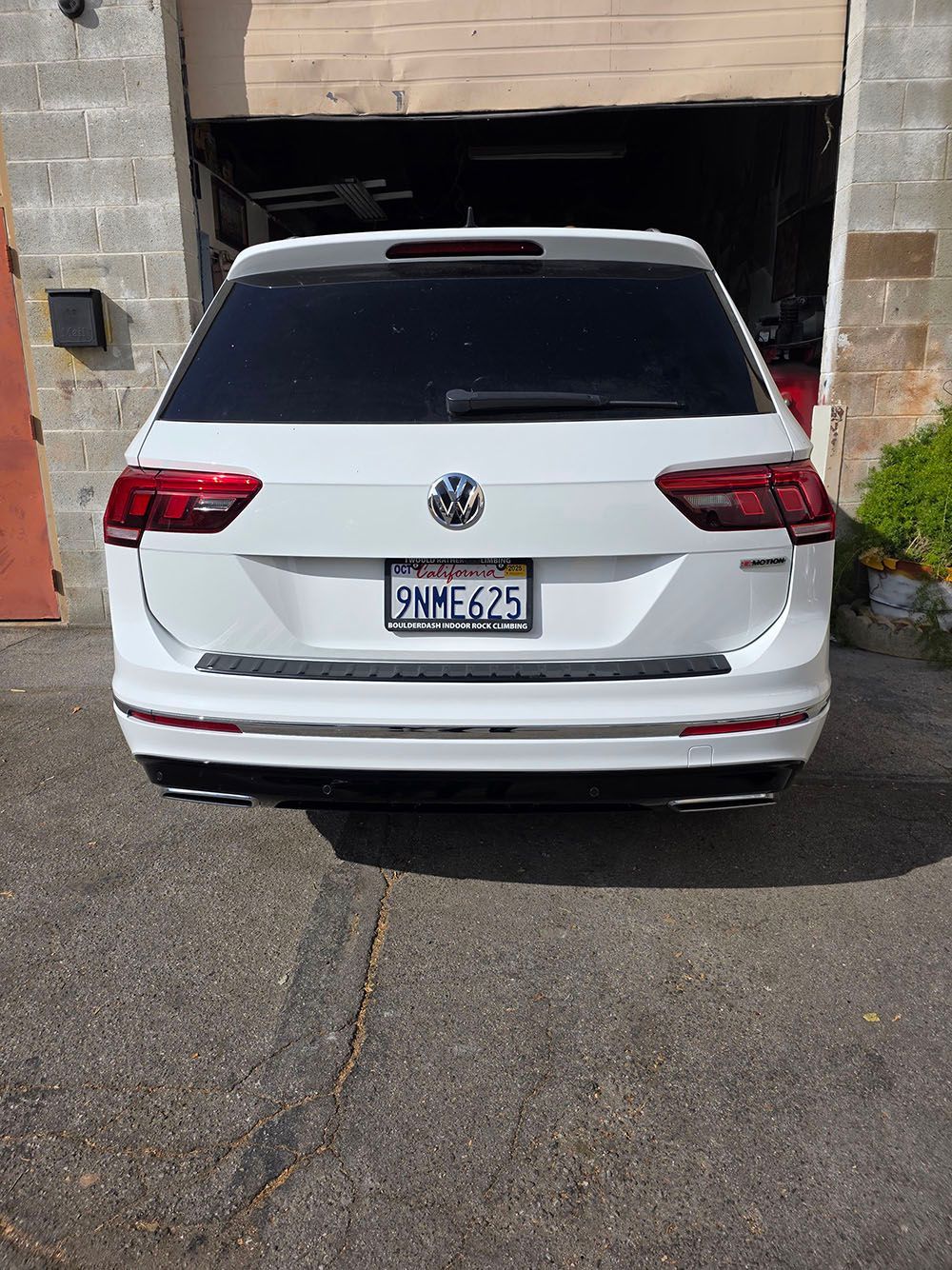 White Volkswagen SUV parked in a garage doorway, rear view.