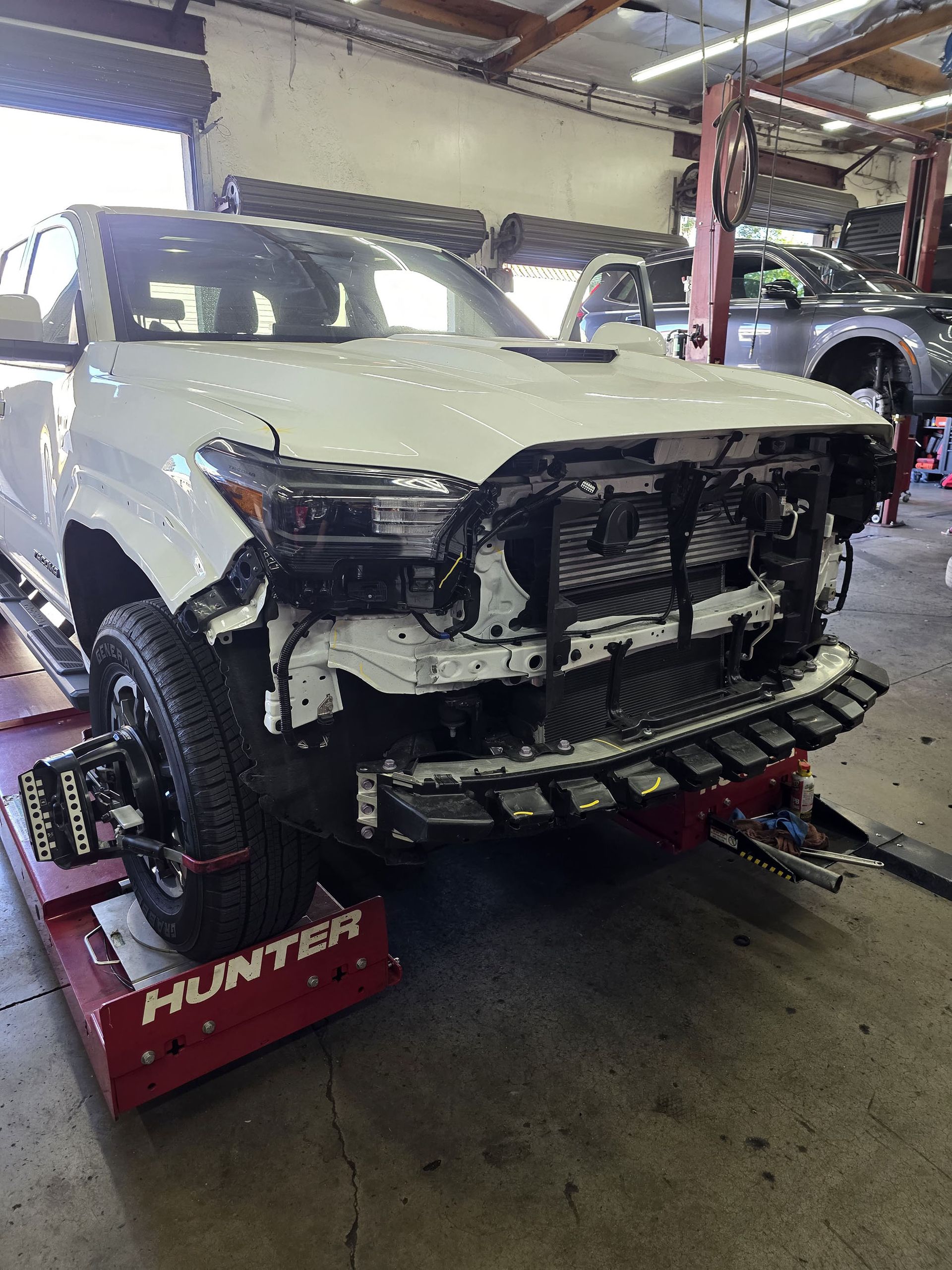White SUV with front-end damage on a red lift in an auto repair shop