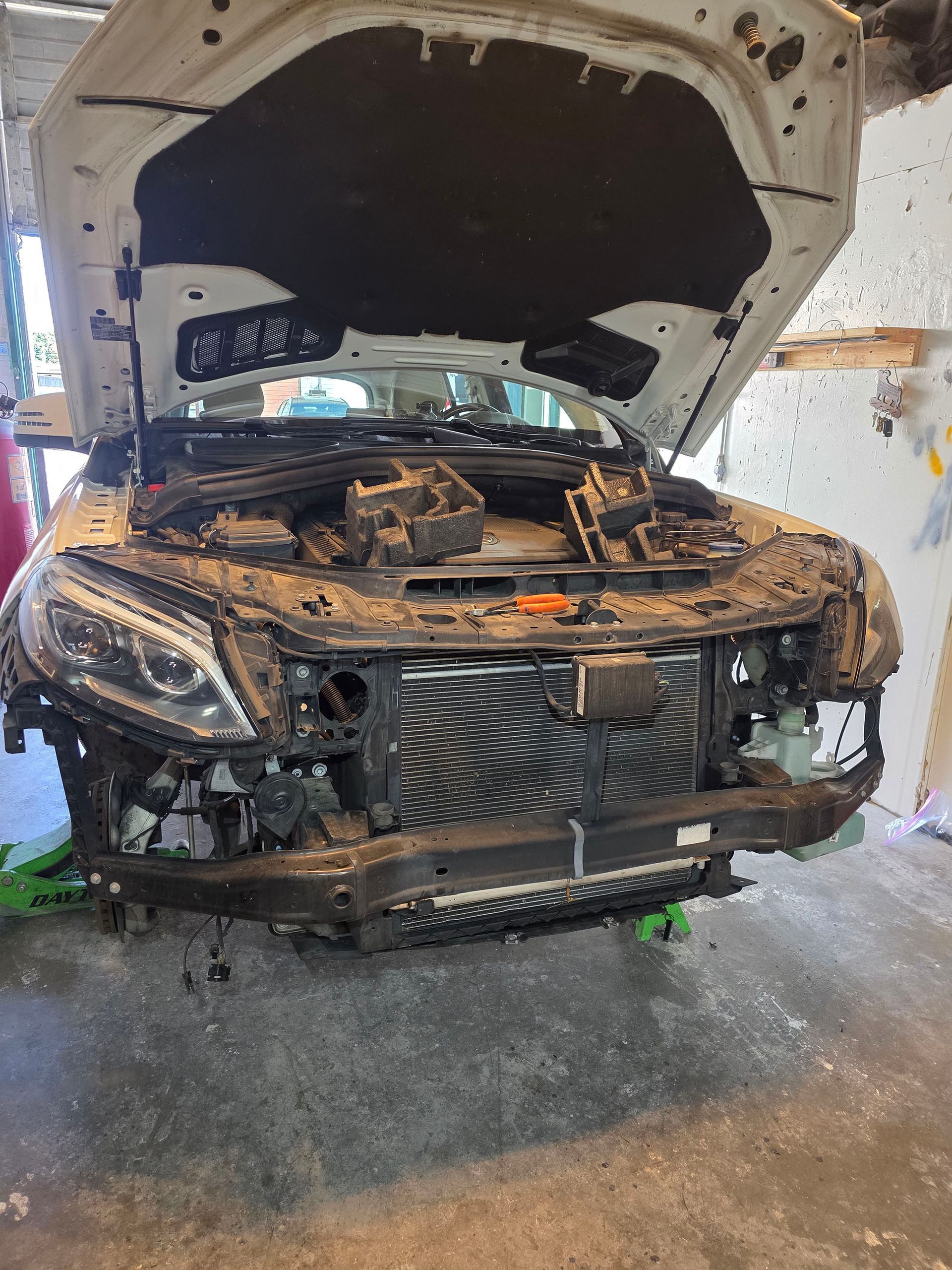 Damaged black car with hood open in a garage, front end heavily crushed and exposed.