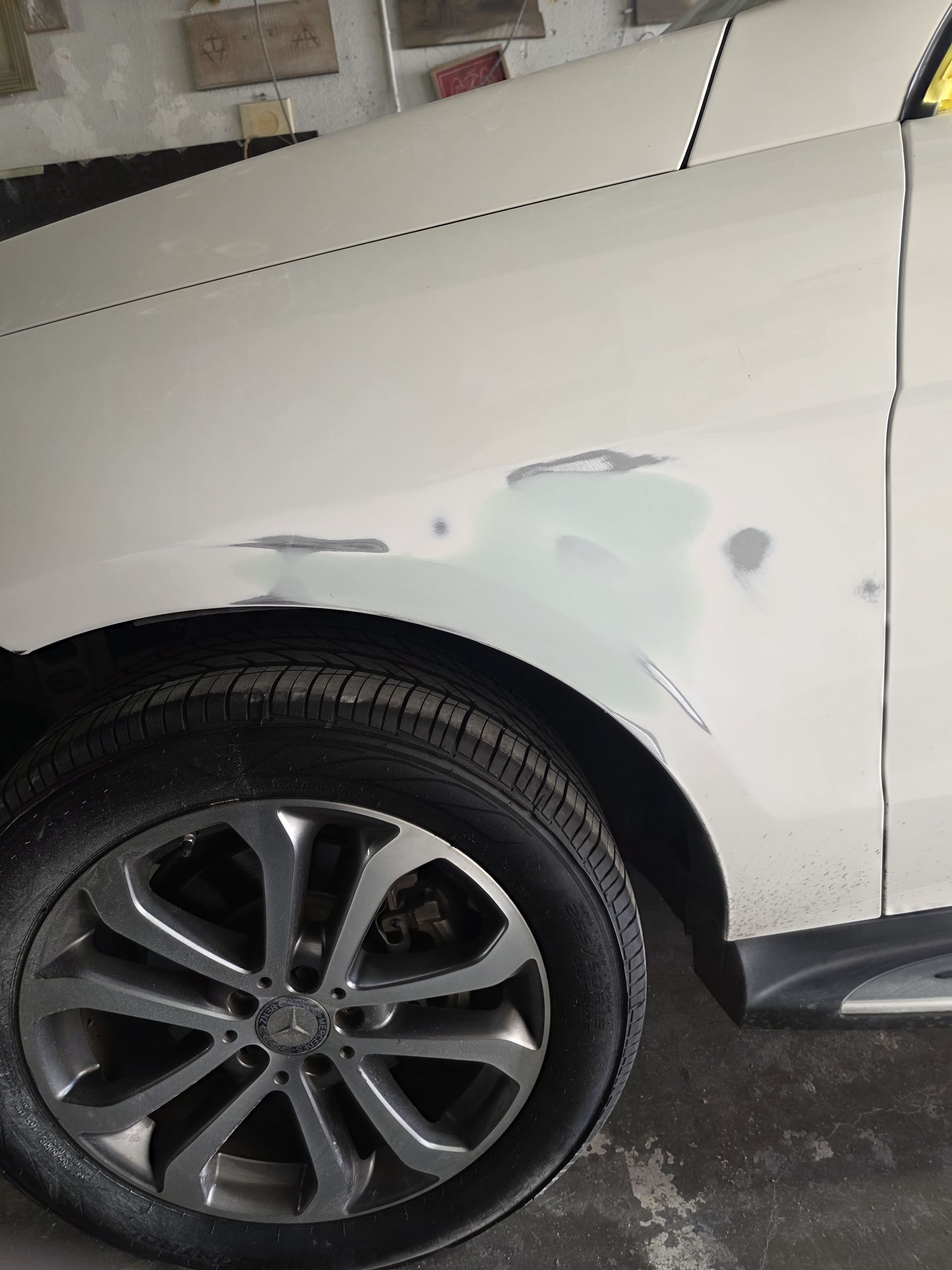 White car with rear wheel and fender damage, showing primer patches on the side panel.