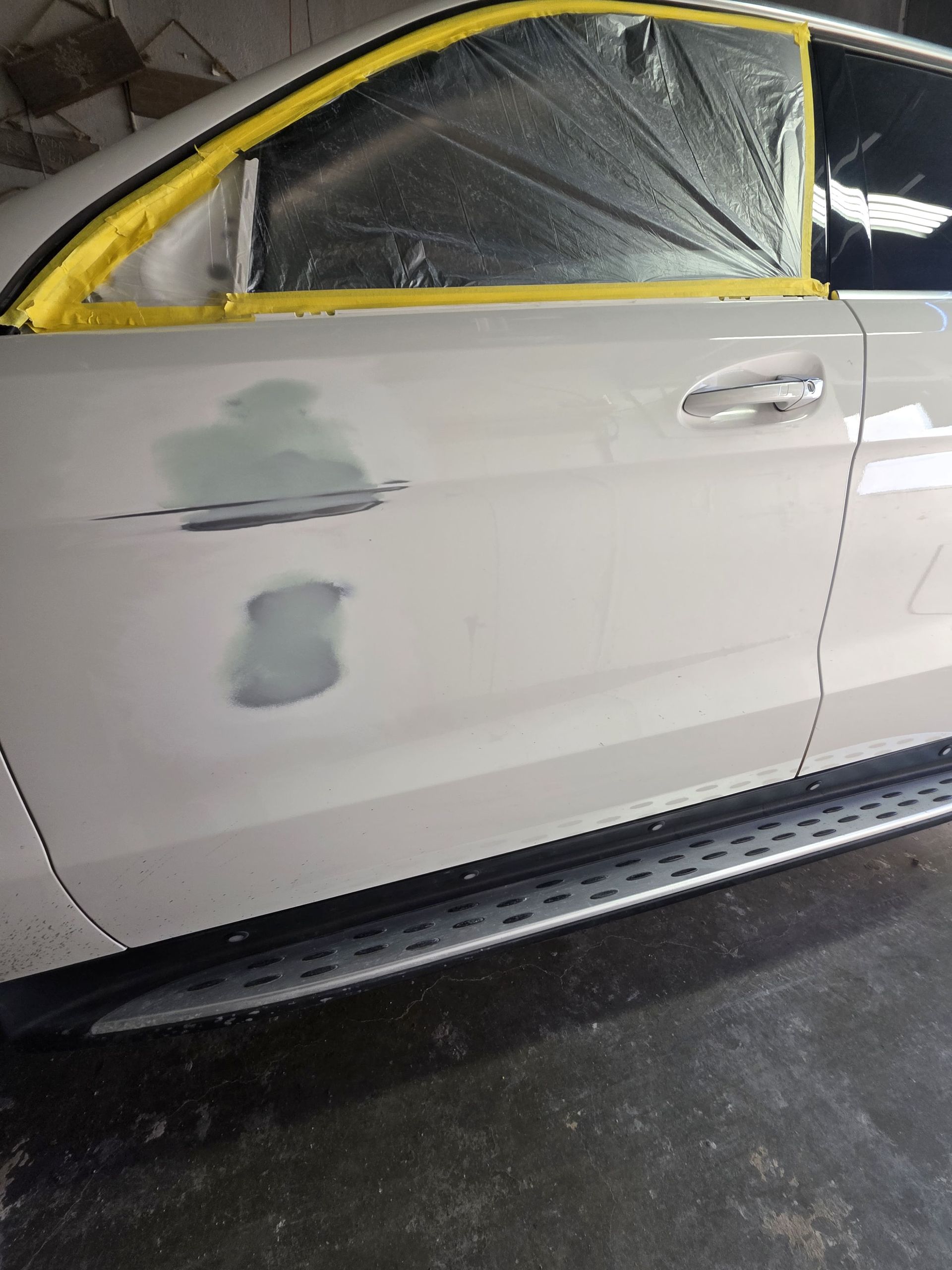 White car with yellow-taped windows and primer patches in an auto body shop