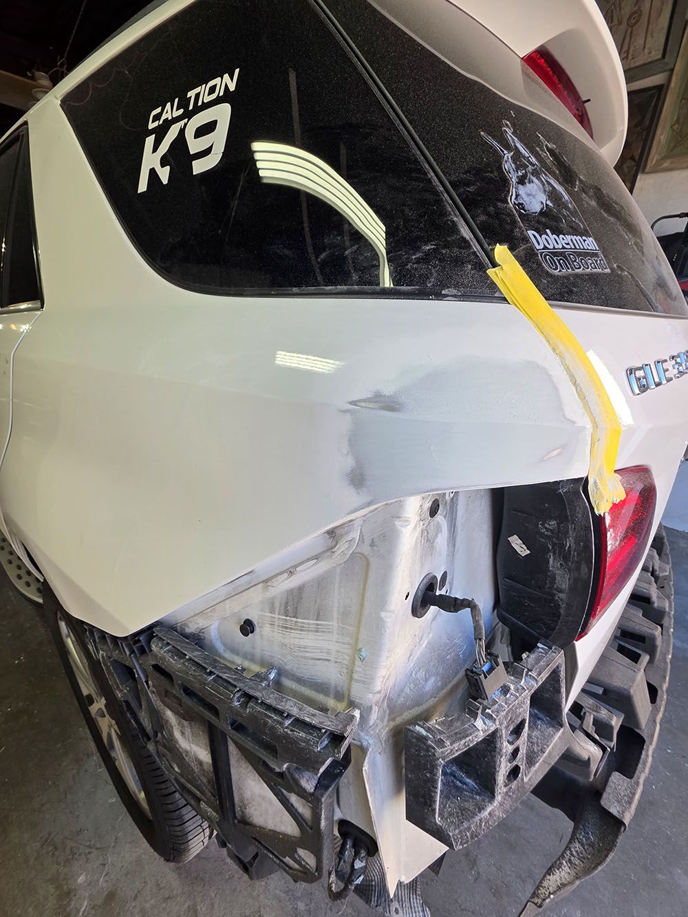 Damaged white K9 vehicle front with broken bumper and cracked windshield in a garage