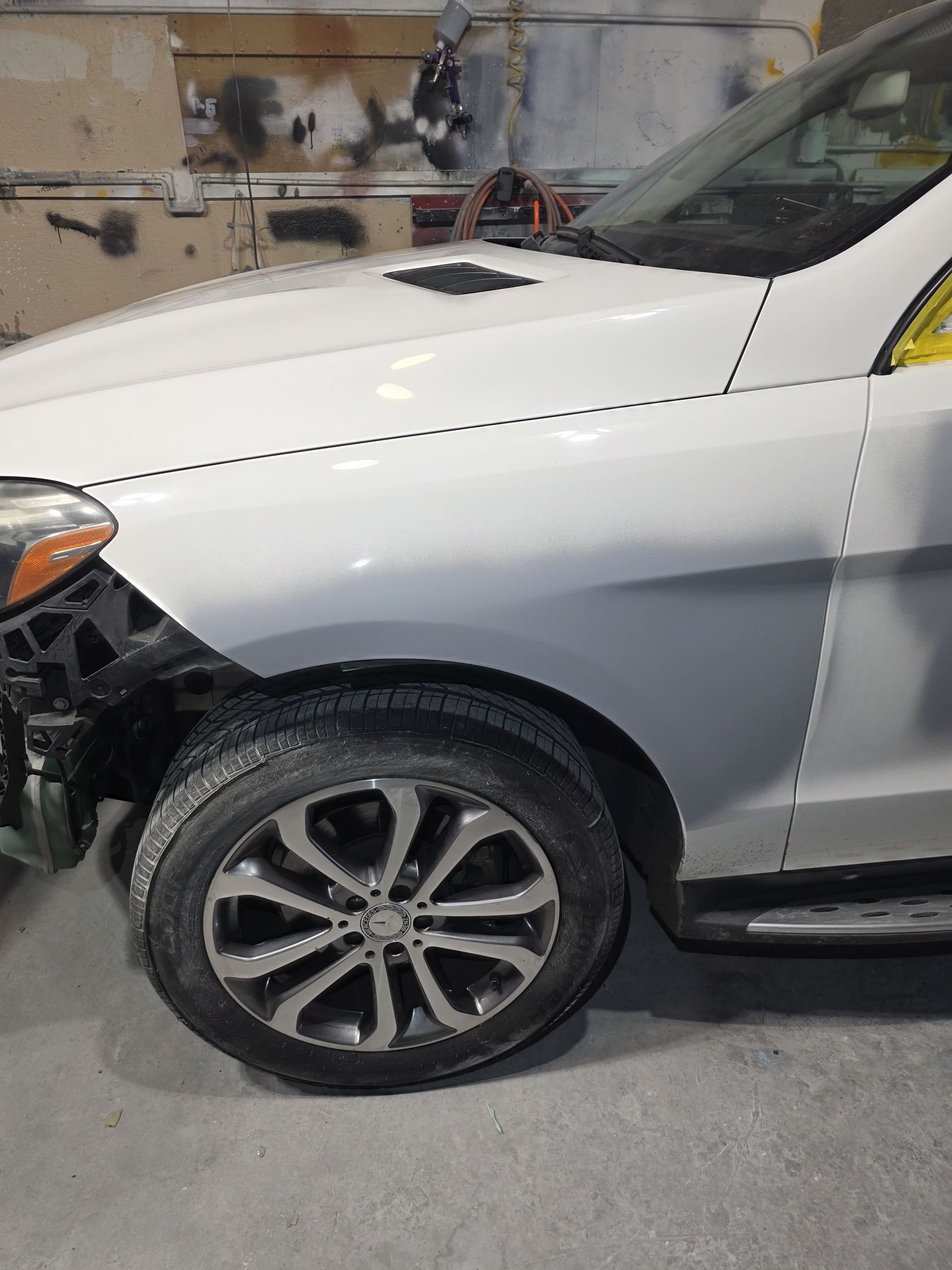 White SUV with front-left fender and bumper damage in a garage, wheel turned outward