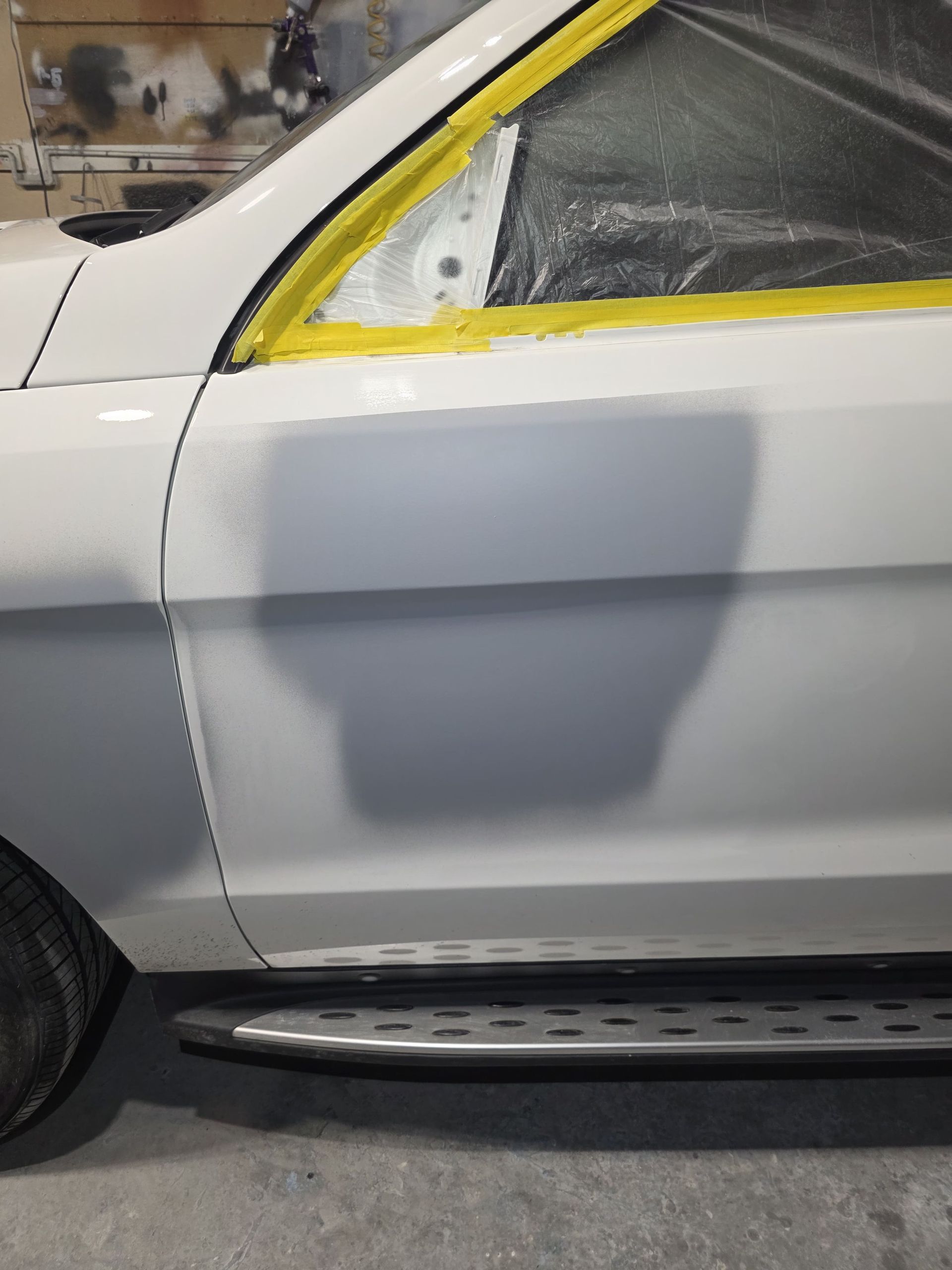 Gray car door with taped window and primer spot, viewed from the side
