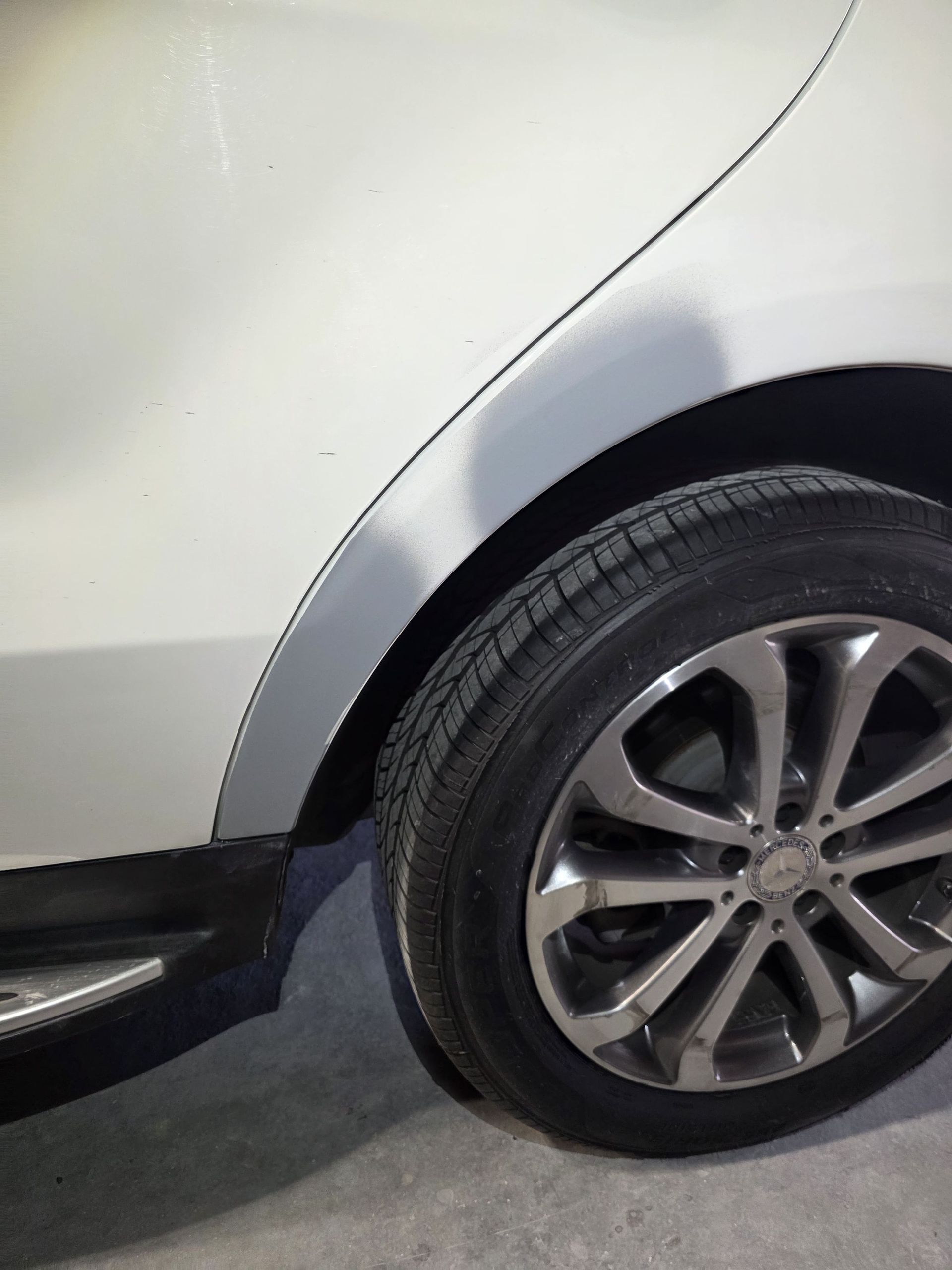 Close-up of a silver car’s rear wheel and fender on a street side.