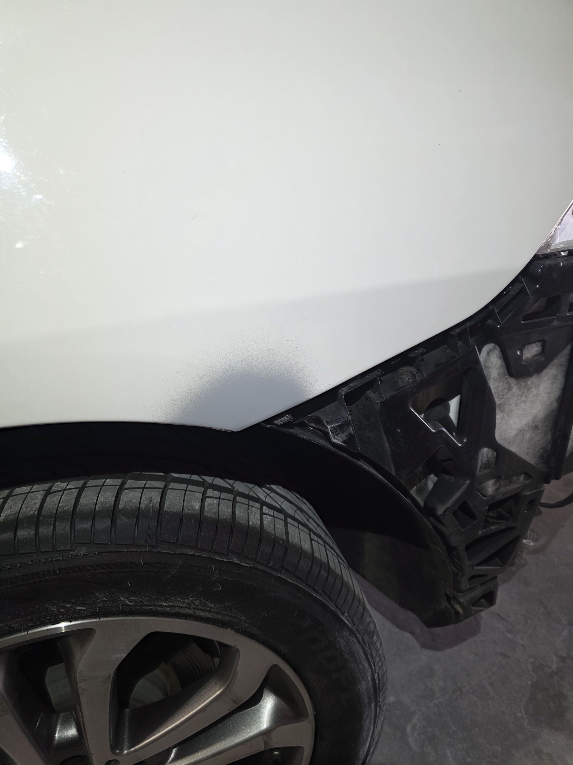 White car rear wheel and damaged black bumper in a parking area