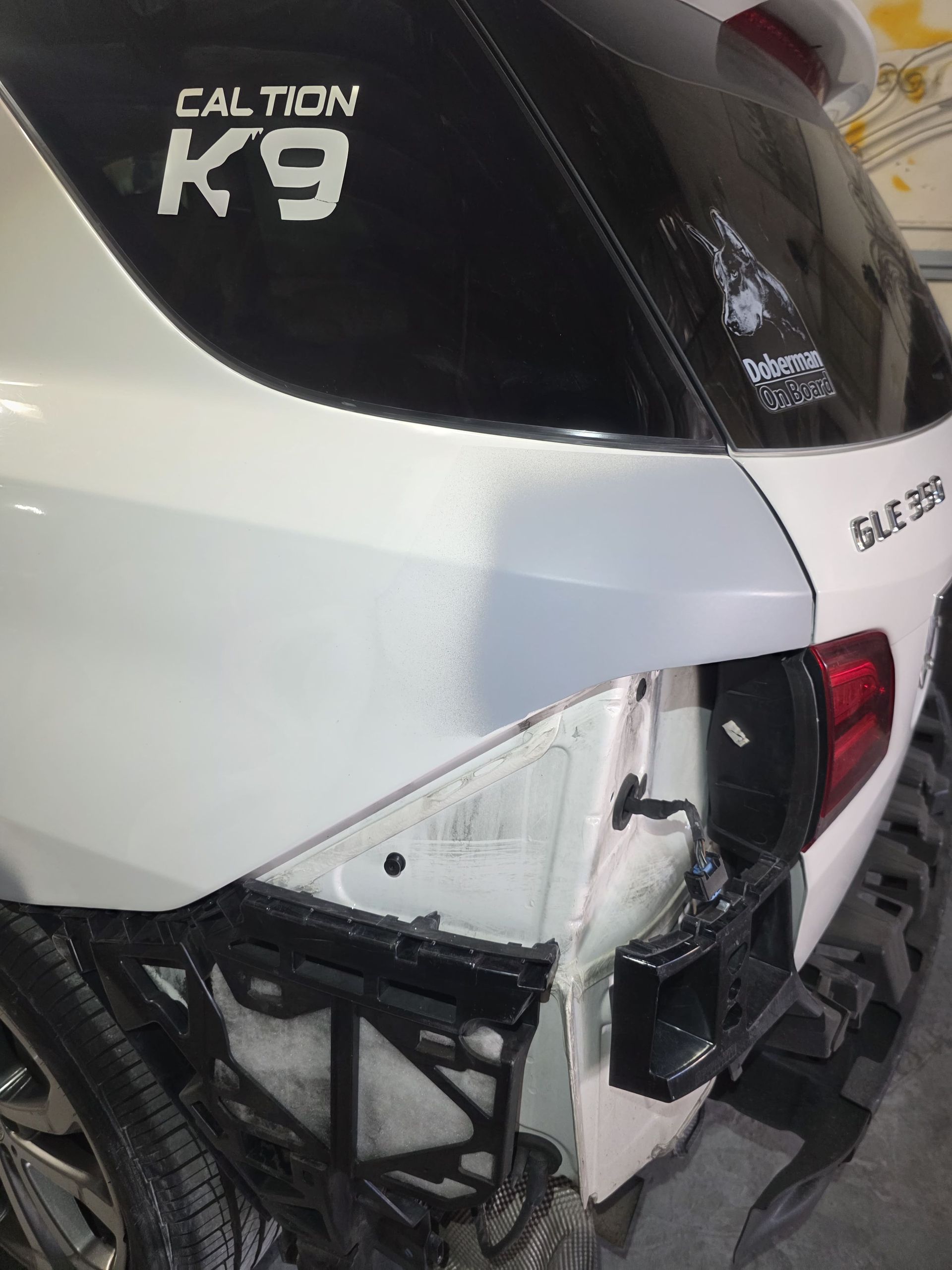 Damaged white SUV rear with broken taillight and crumpled bumper, CALTIGN K9 decal visible
