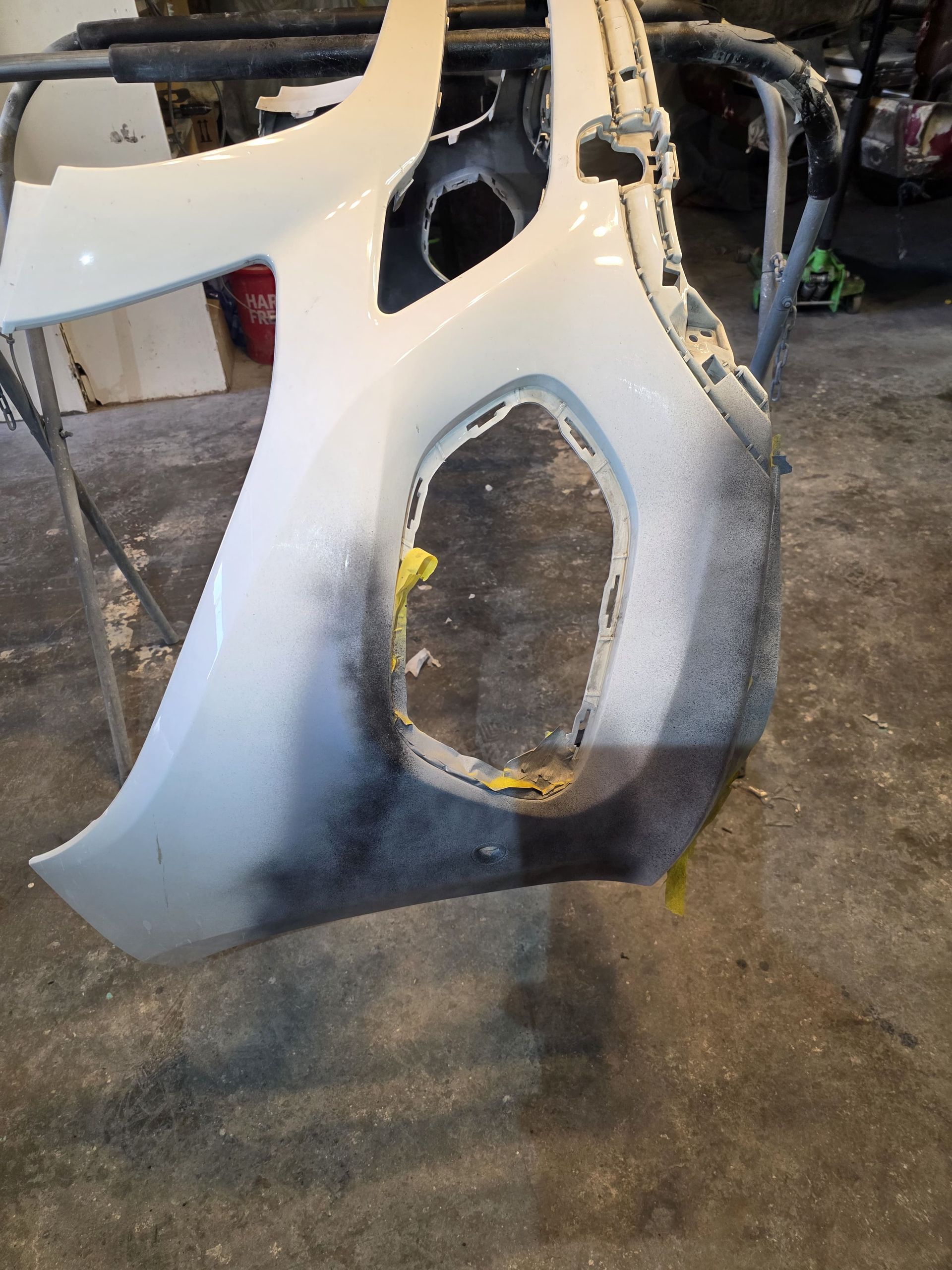 White car body panel hanging in a workshop, with a large cutout and dark primer marks near the bottom.