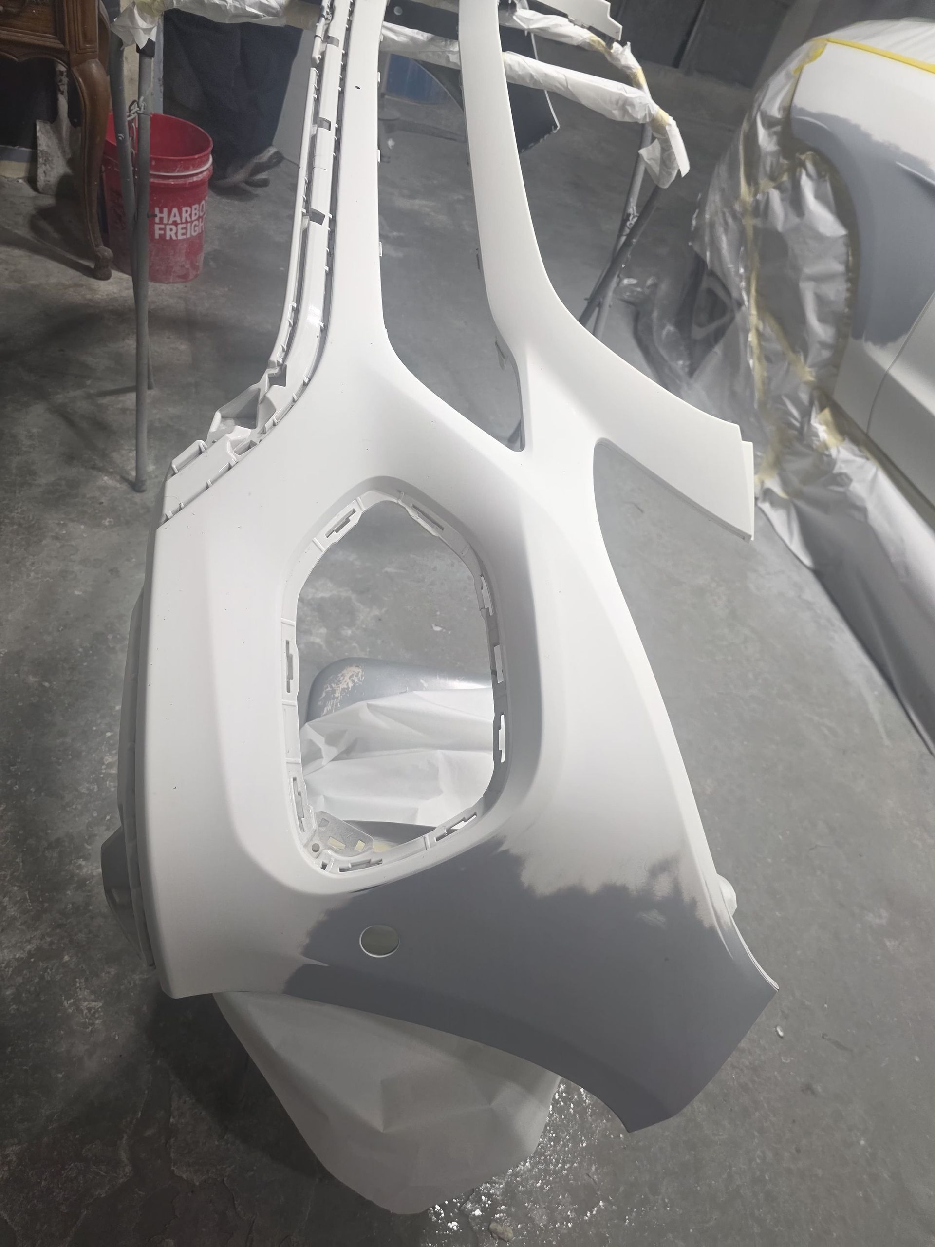 White and gray car body panel in a workshop, with a large opening and unfinished edges