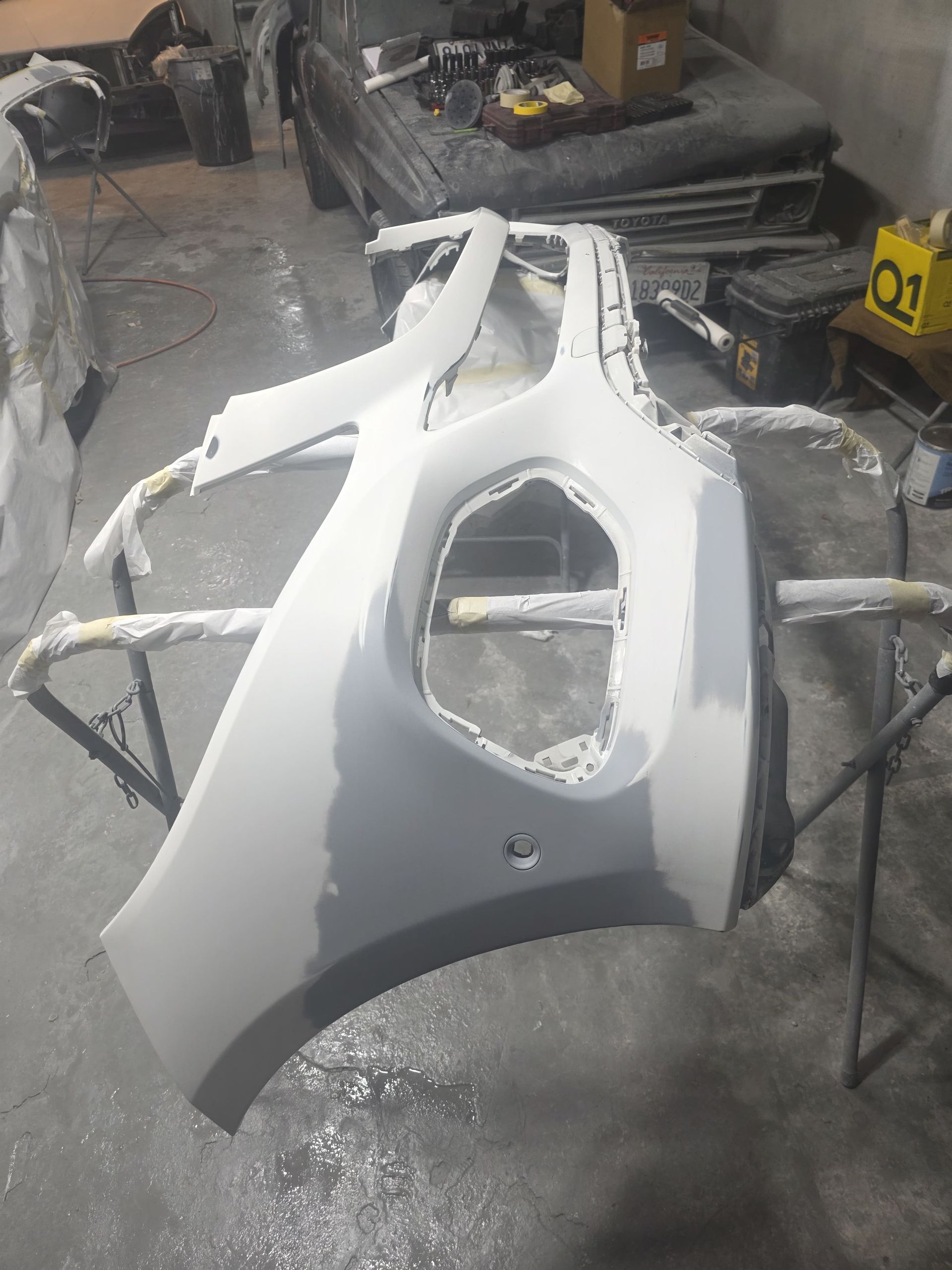 White car body panel with a large opening, resting in a workshop on metal stands.