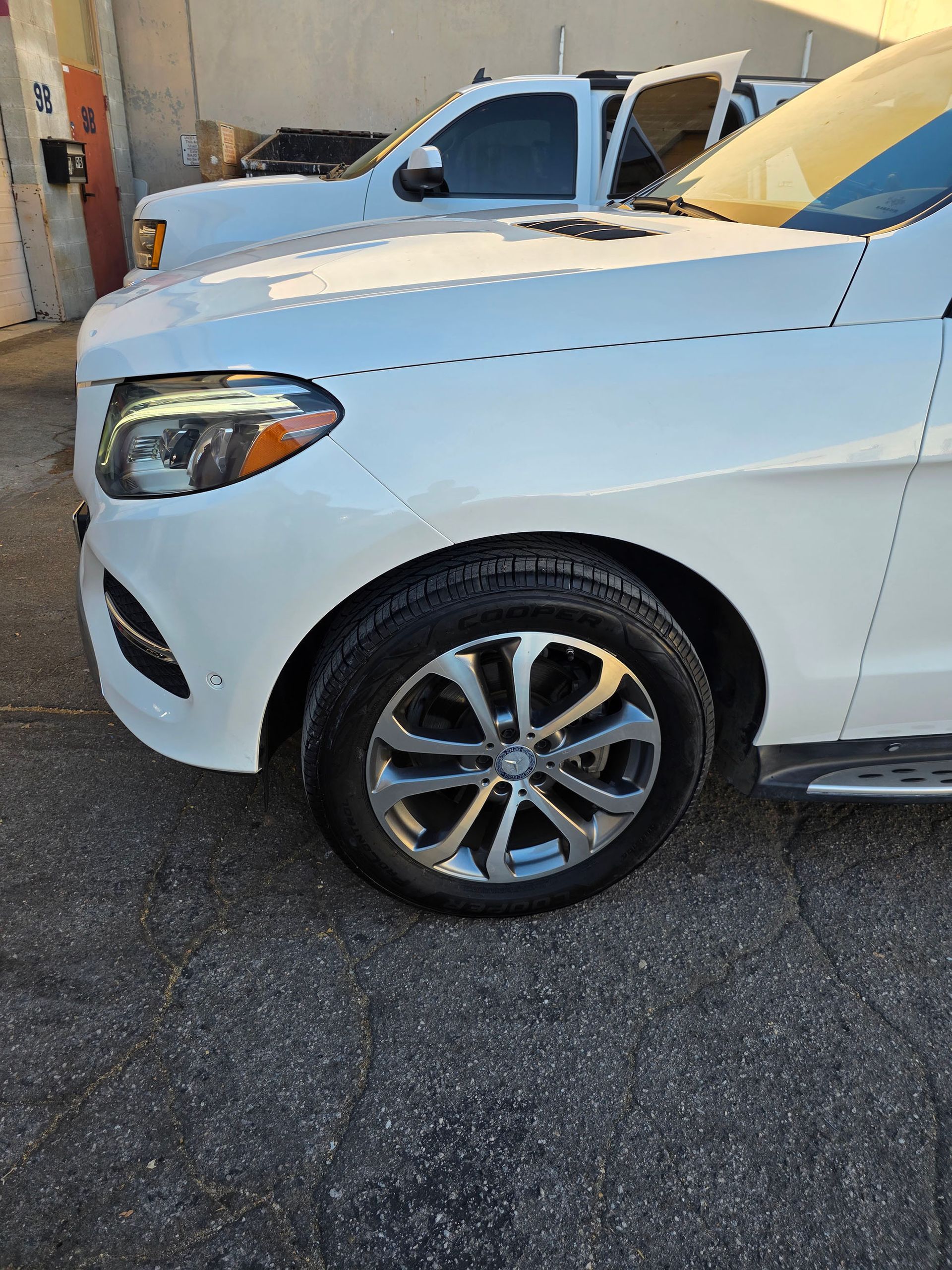 White SUV parked outdoors beside a building, front side view with another vehicle behind it