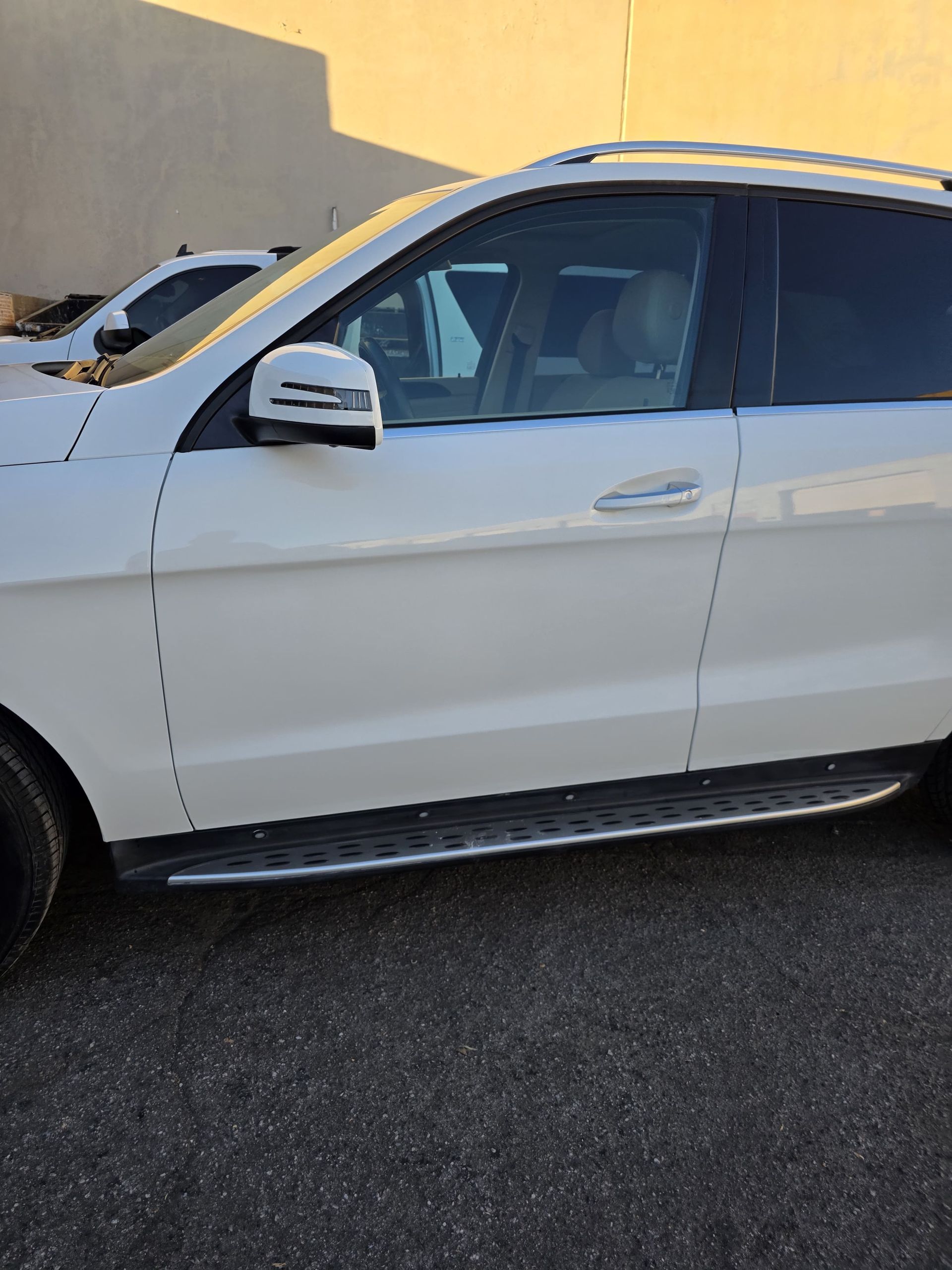 White SUV parked beside a building, side view with tinted windows and running board