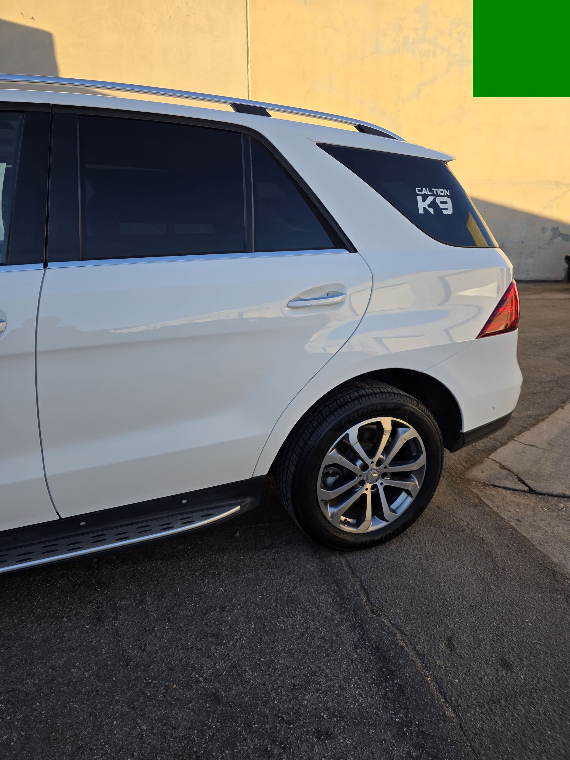 White SUV parked beside a yellow wall on a street, rear side view.