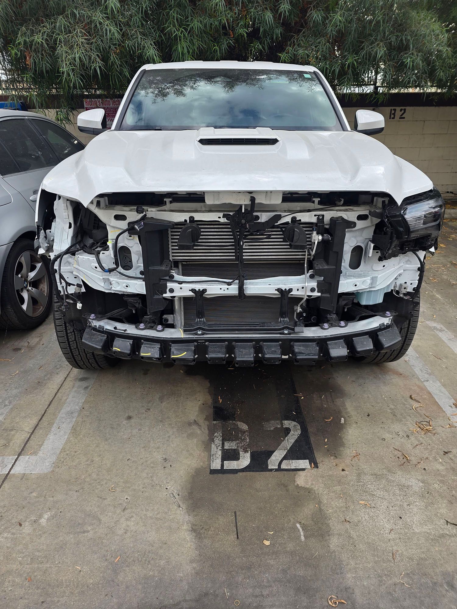 White SUV with front-end damage parked in a lot, missing grille and bumper, over parking space B2.