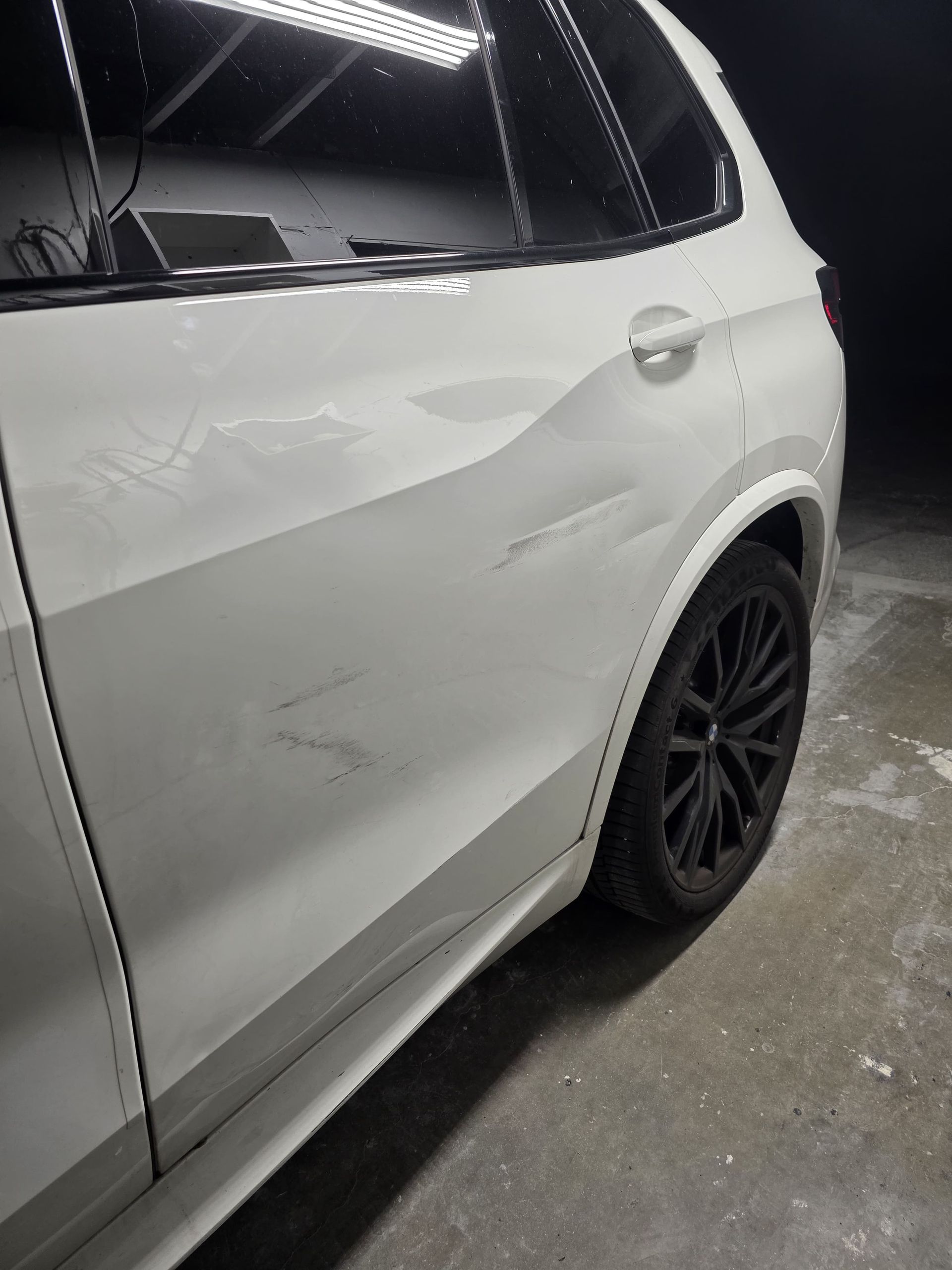 White SUV with black wheels and visible side dents in a dimly lit garage.