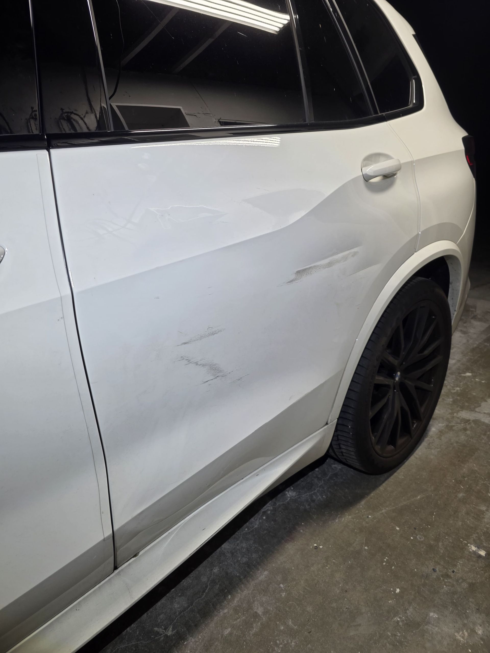 White SUV with a dent and scuff marks on the side door and panel in a garage