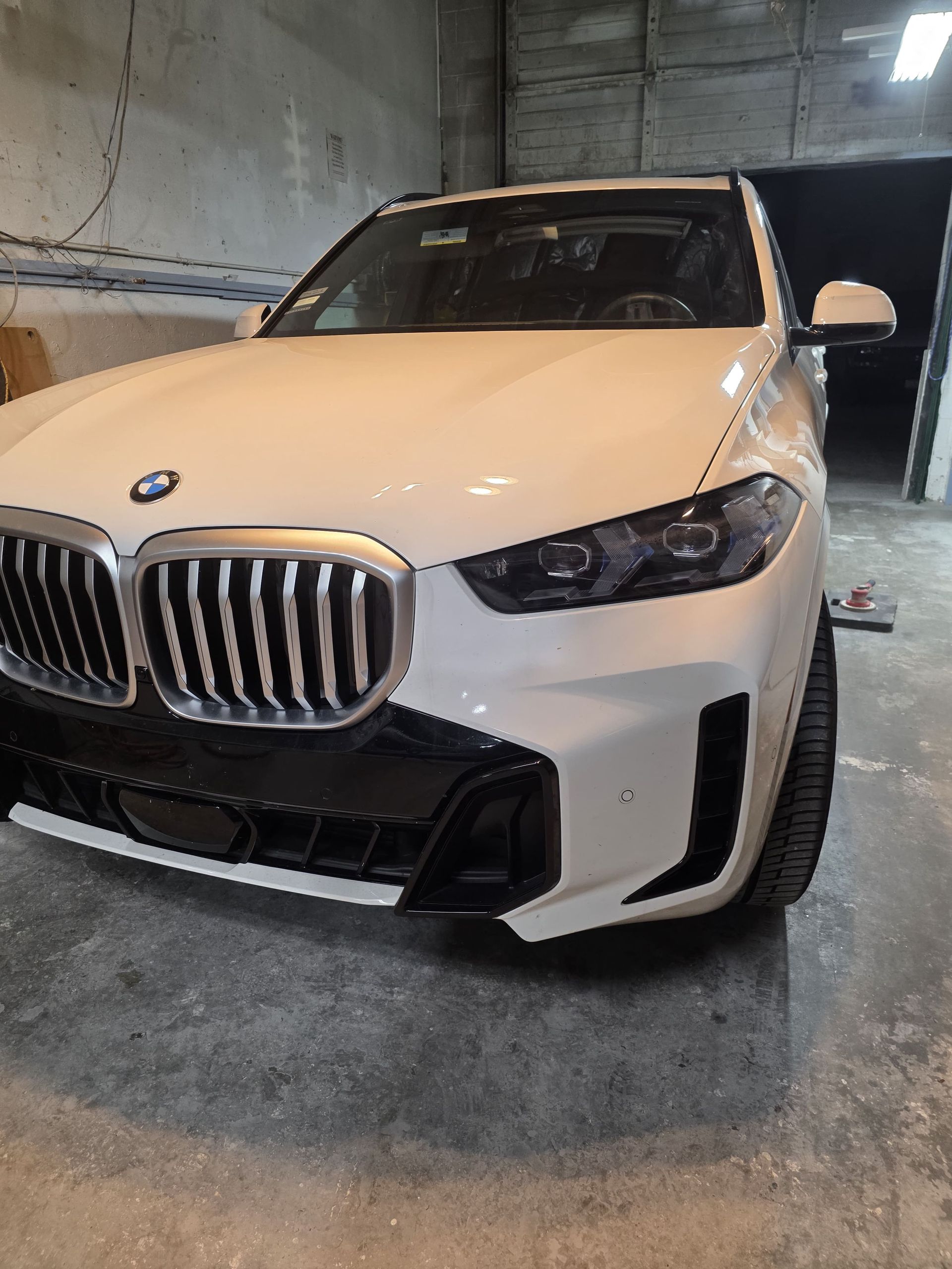 White BMW SUV parked indoors in a dim garage, front view.