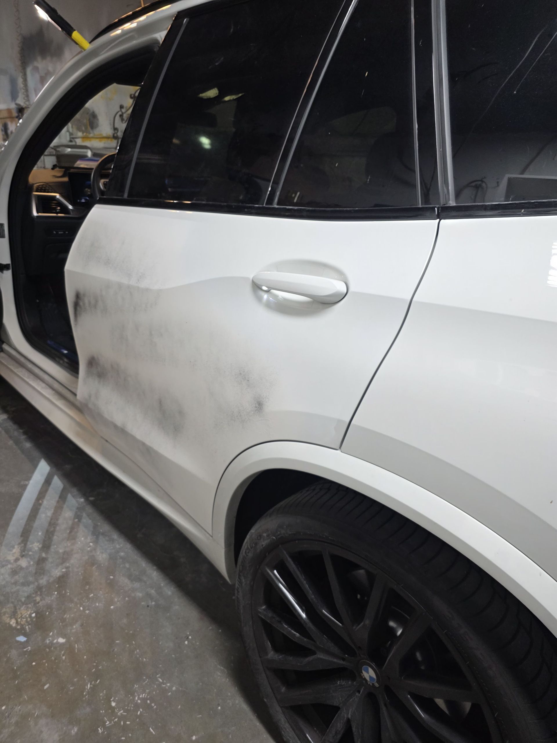 White SUV with a dirty side door and black wheel, parked in a garage with the door open