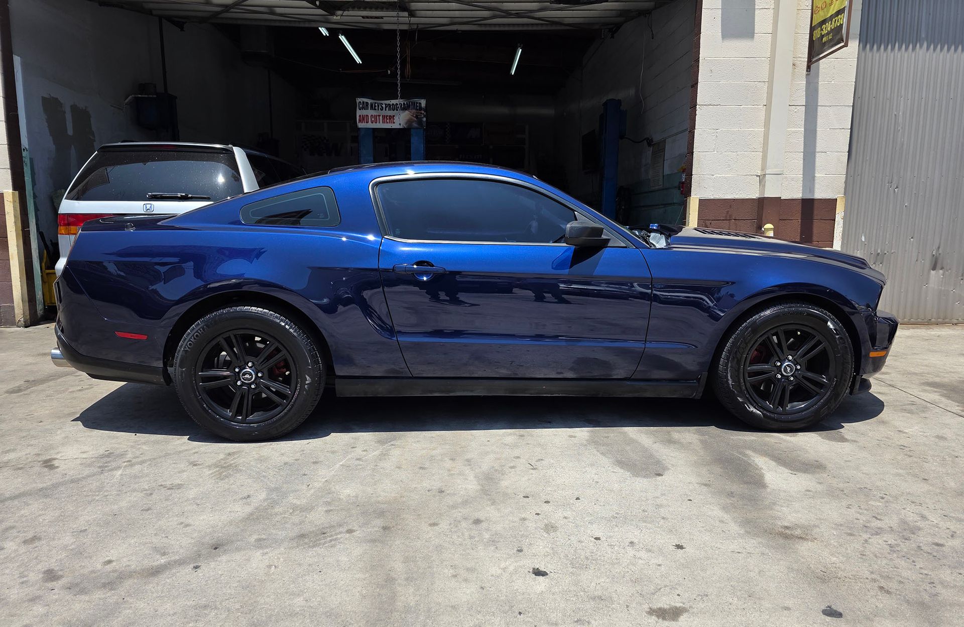 Blue sports coupe parked outside a garage, side view, with black wheels.