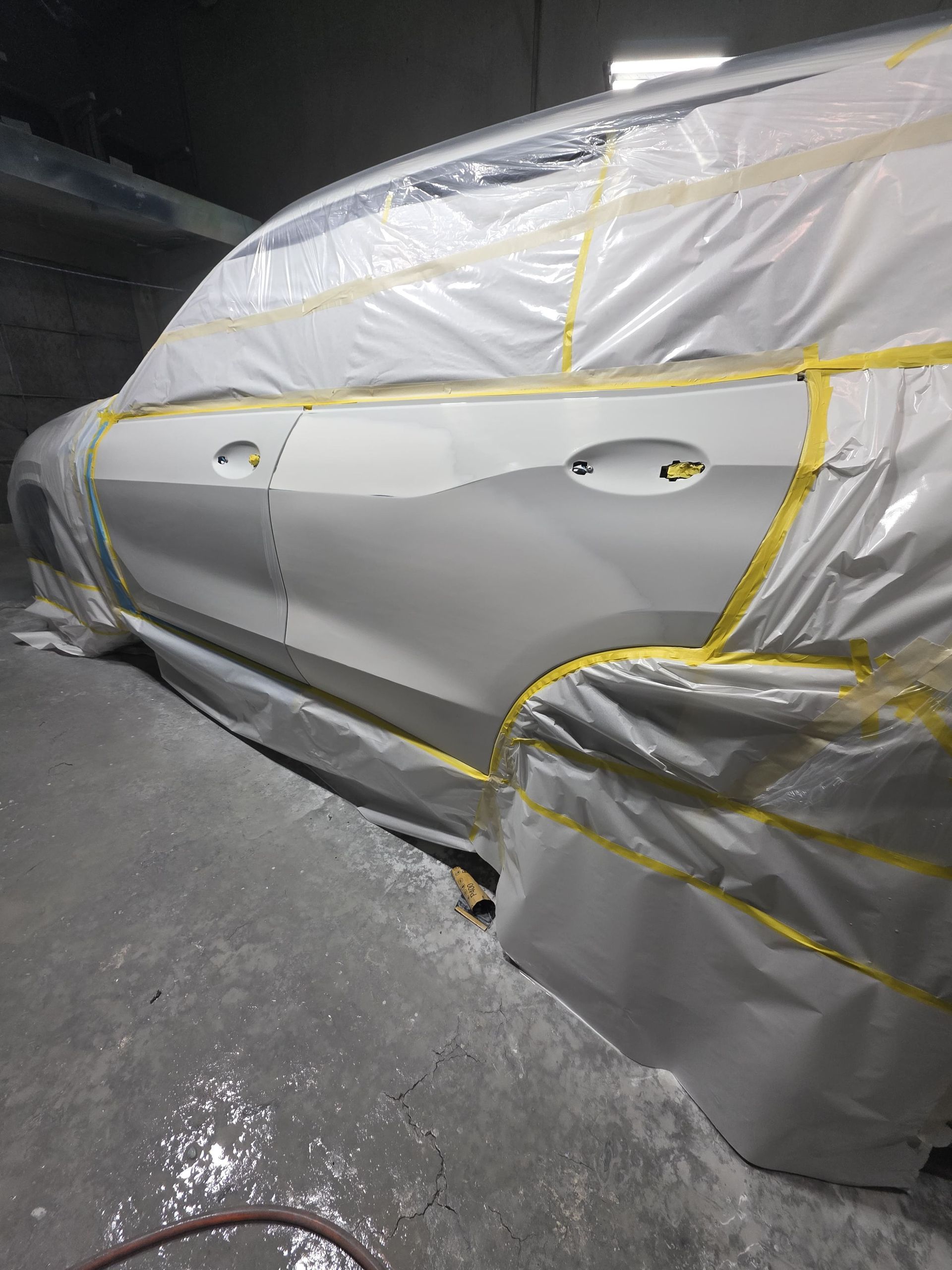 Car covered in protective plastic sheeting and tape in a dim garage or repair shop