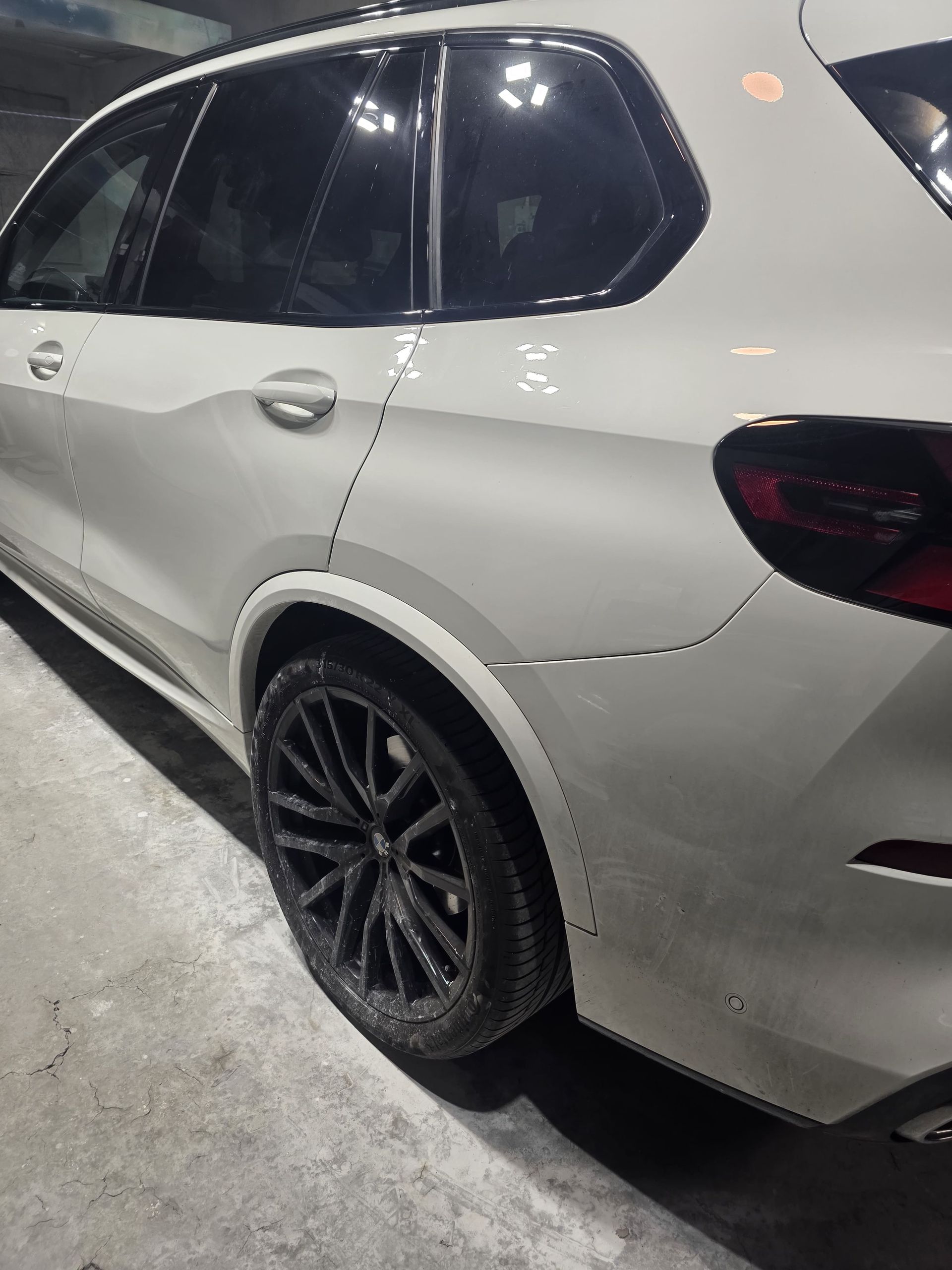 White SUV with black rims parked in a garage, viewed from the rear side.