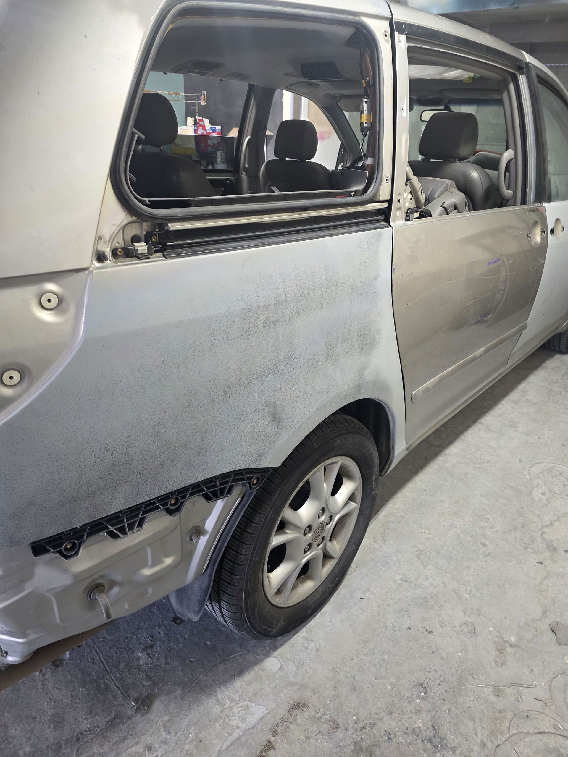 Damaged silver minivan with broken rear side window and dented body in a garage