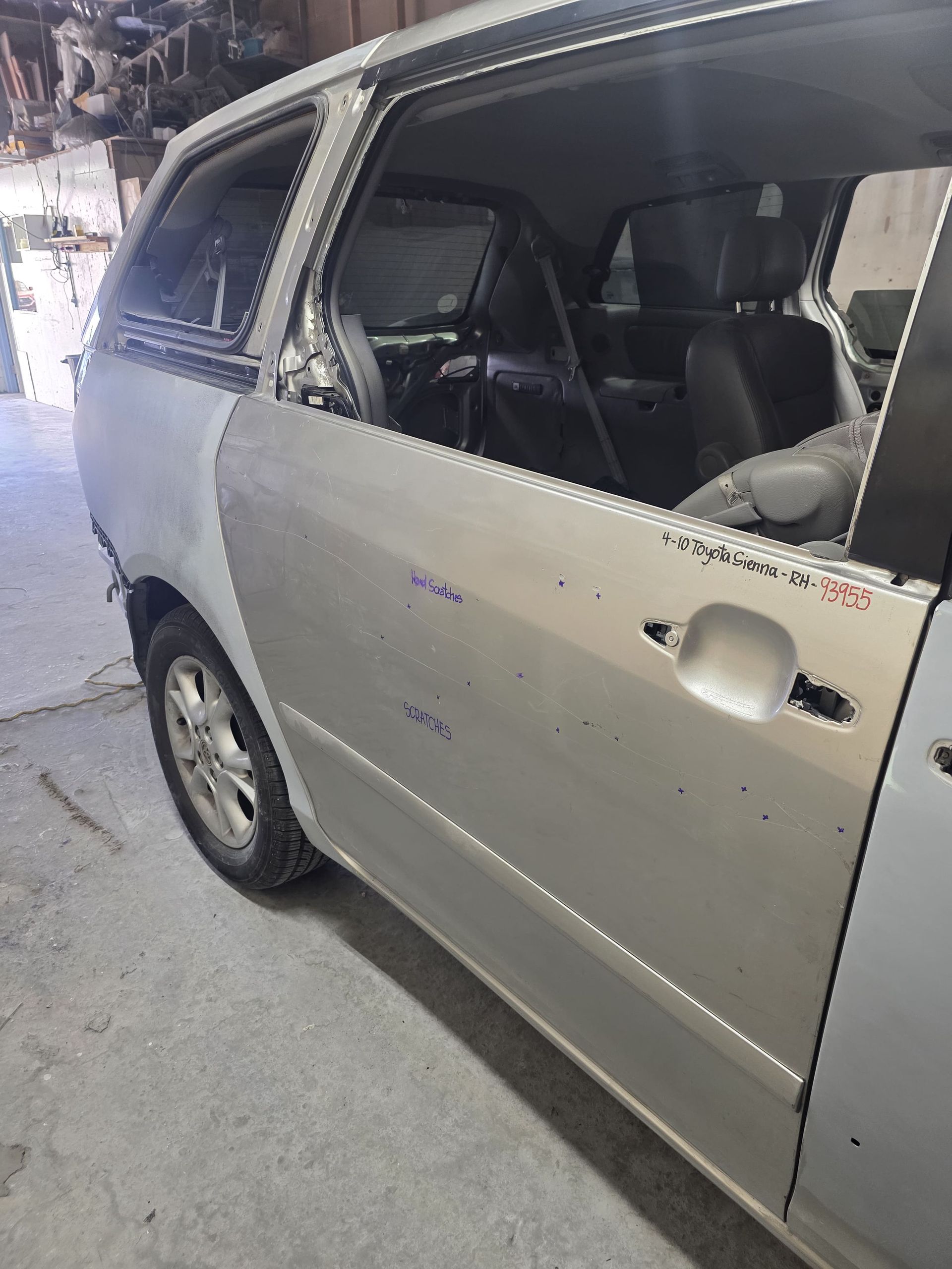 Damaged silver minivan with shattered side windows in a garage or repair shop