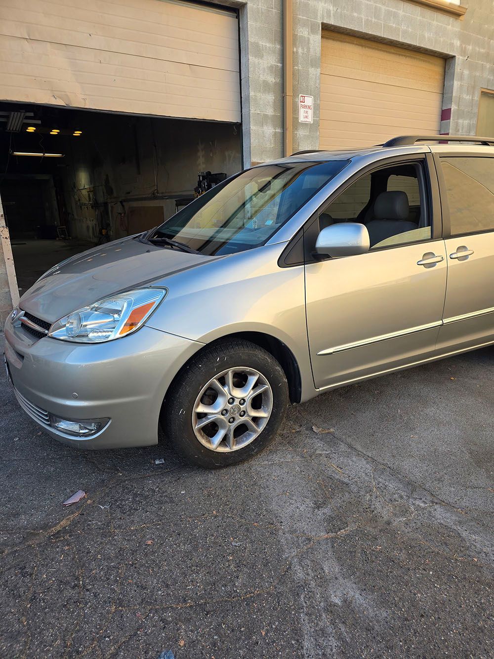 Silver minivan parked outside a garage on a city street