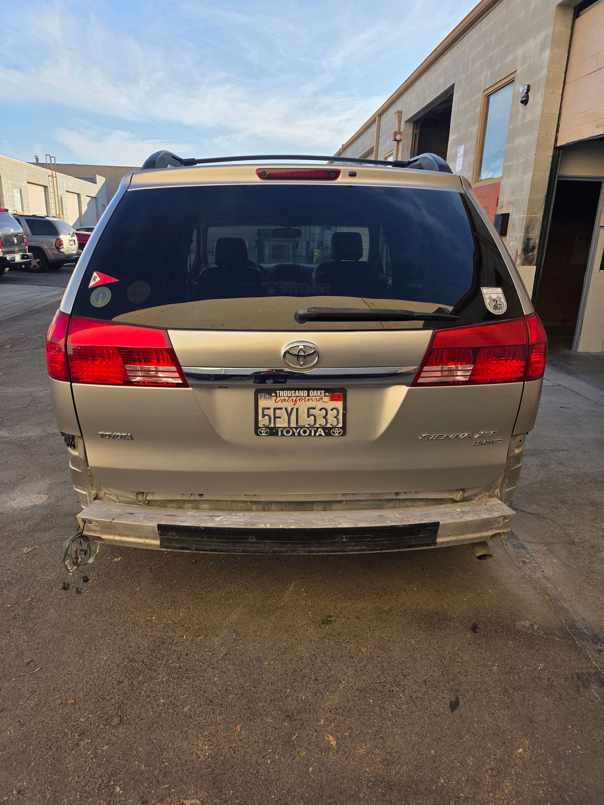 Rear view of a beige minivan parked beside industrial buildings on a wet lot