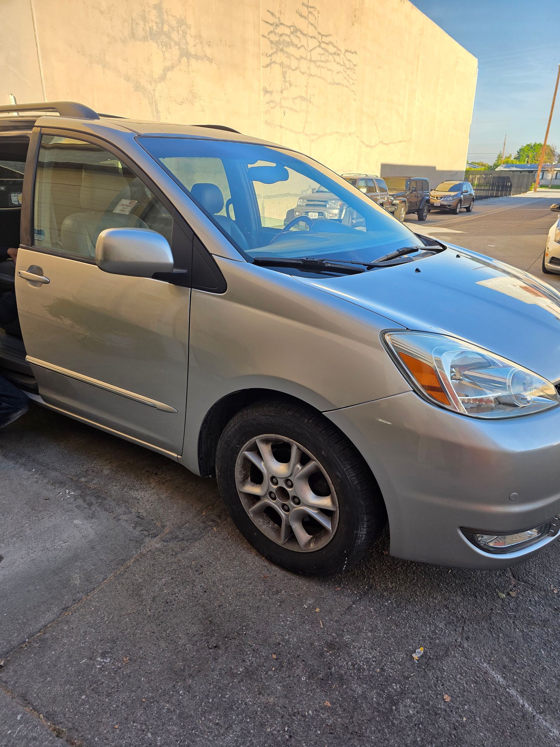 Silver minivan parked on a street beside a beige building in daylight