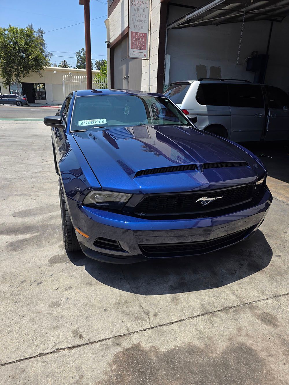 Blue Ford Mustang parked outside a garage on a sunny day