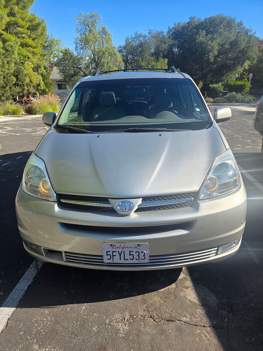 Silver minivan parked in a sunlit lot with trees in the background.