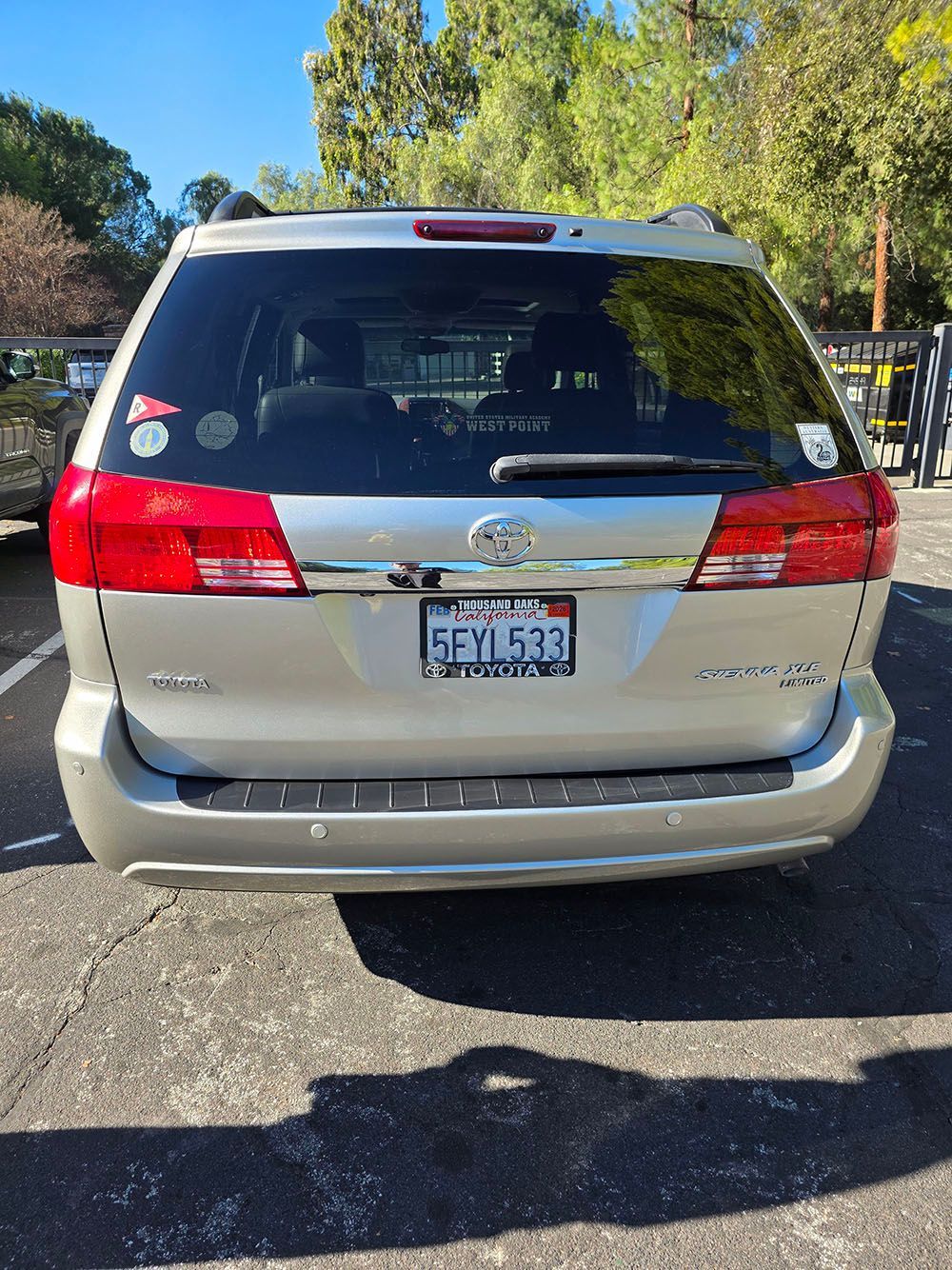 Rear view of a silver SUV parked on a sunny street with trees in the background.