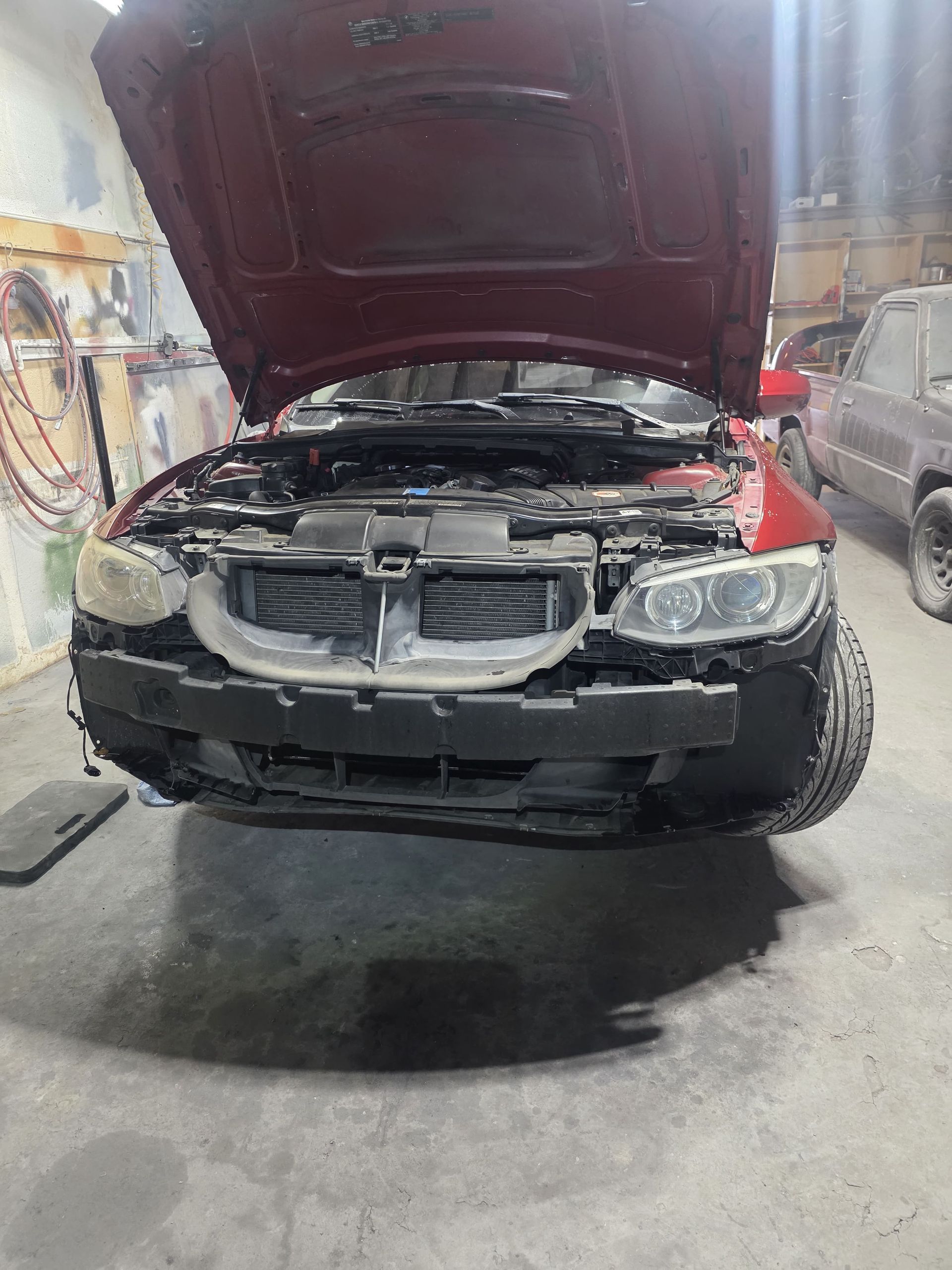 Damaged black car in a repair shop with hood open and front bumper removed
