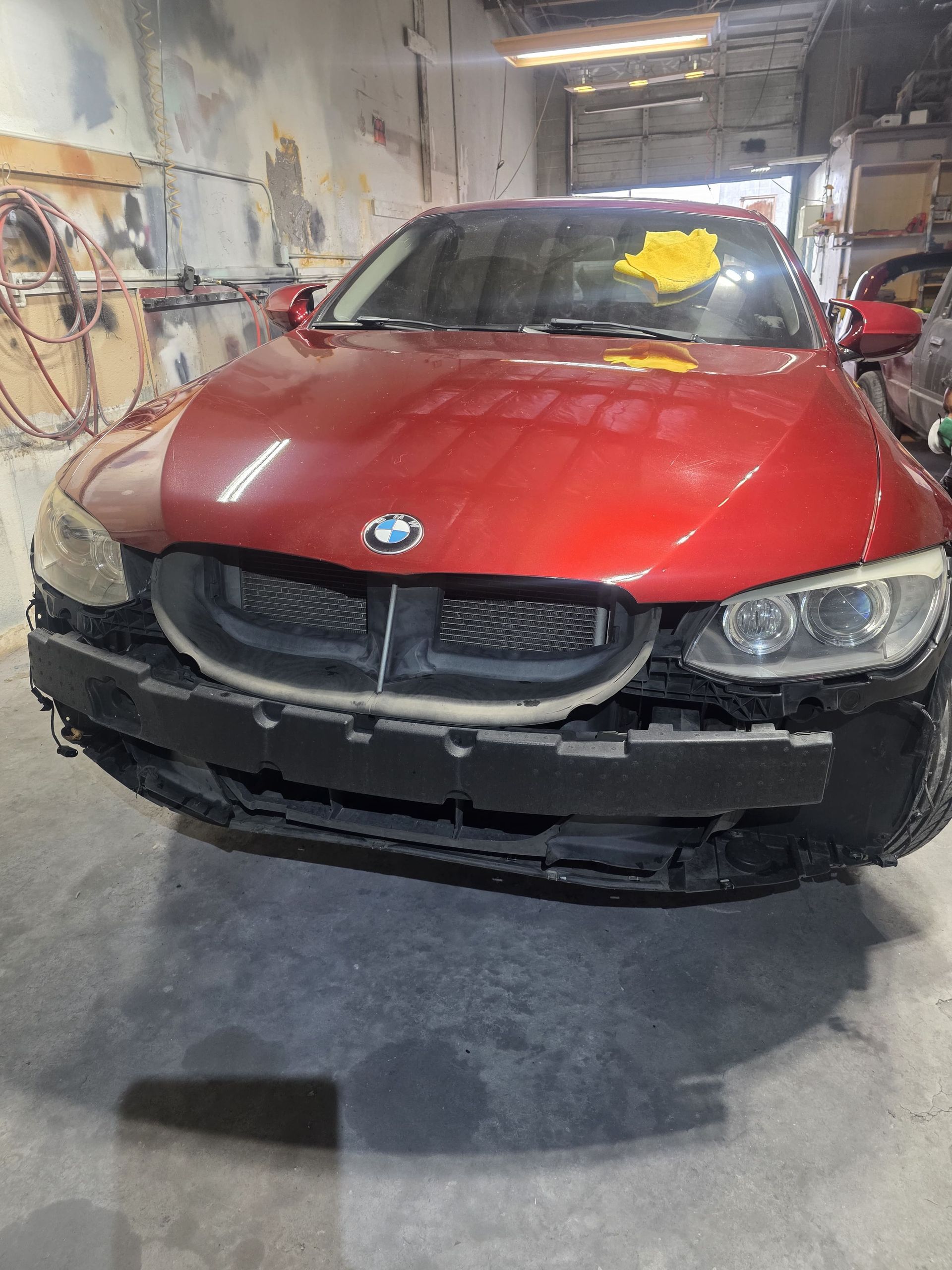 Red BMW with front-end damage parked in an auto body shop.