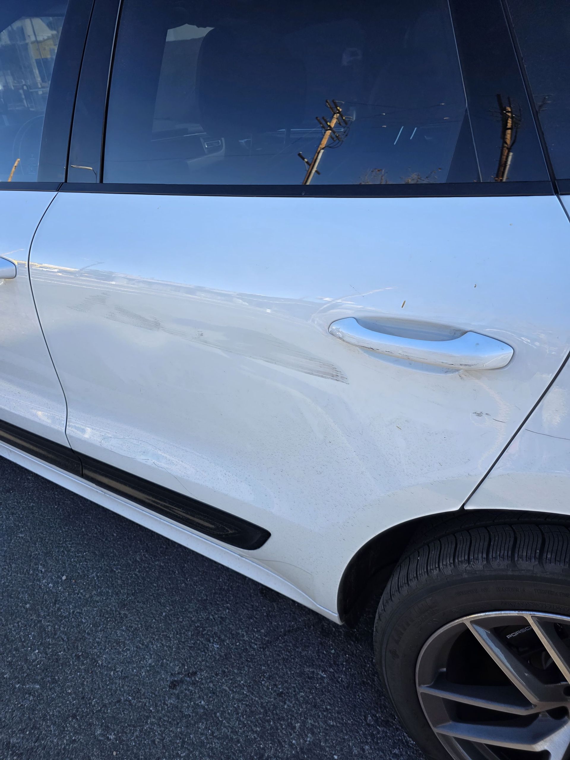White SUV side panel with a dent and scratches near the rear door and wheel.