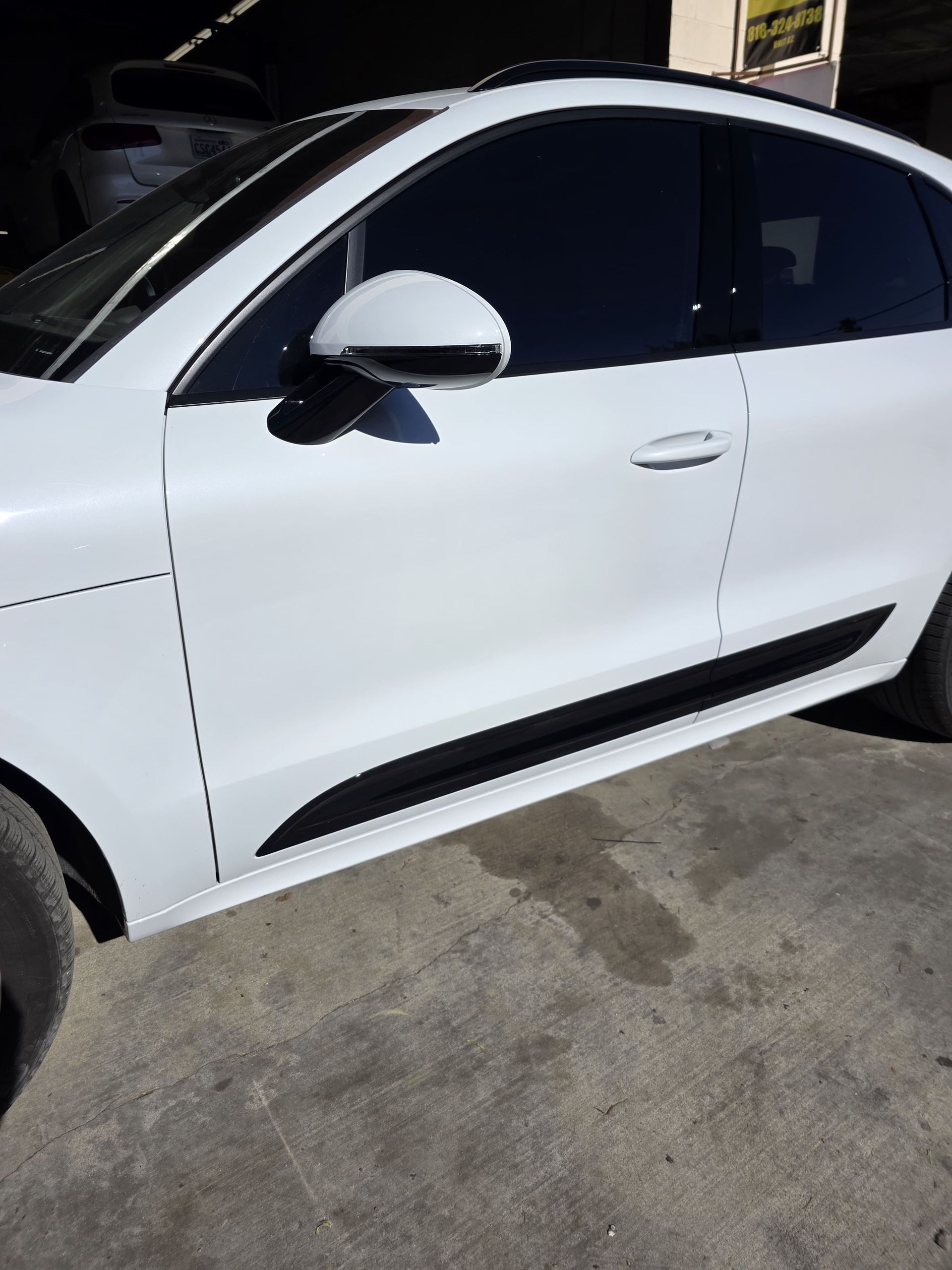 White sedan parked in a garage, side view with tinted windows and black trim