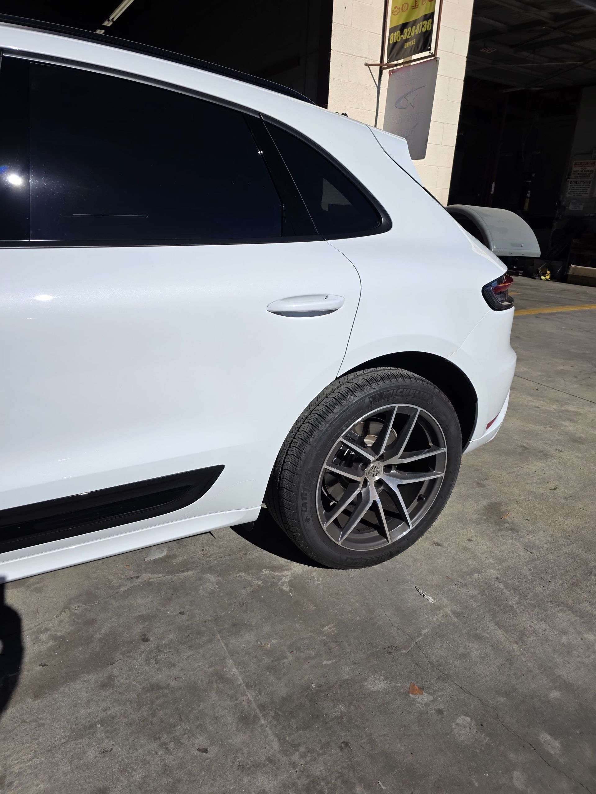 White SUV parked outside a garage, showing the side and rear wheel.
