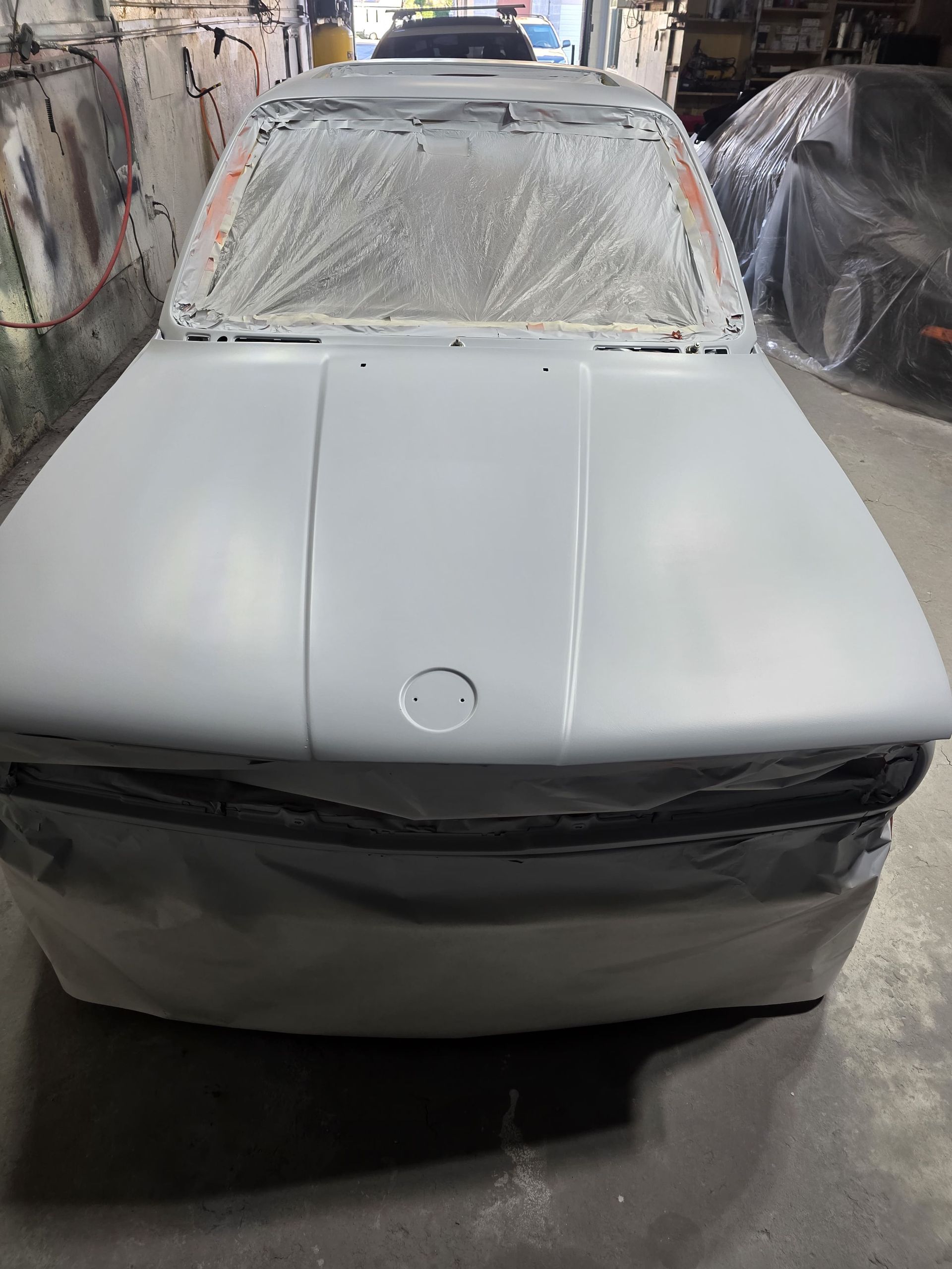 White sedan in a paint booth, covered in primer and ready for refinishing
