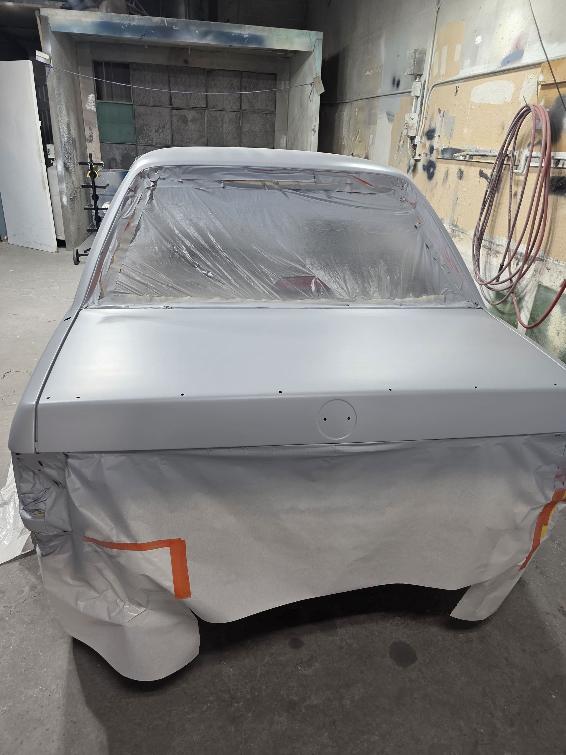 Silver car body in a paint booth, masked with plastic and ready for painting