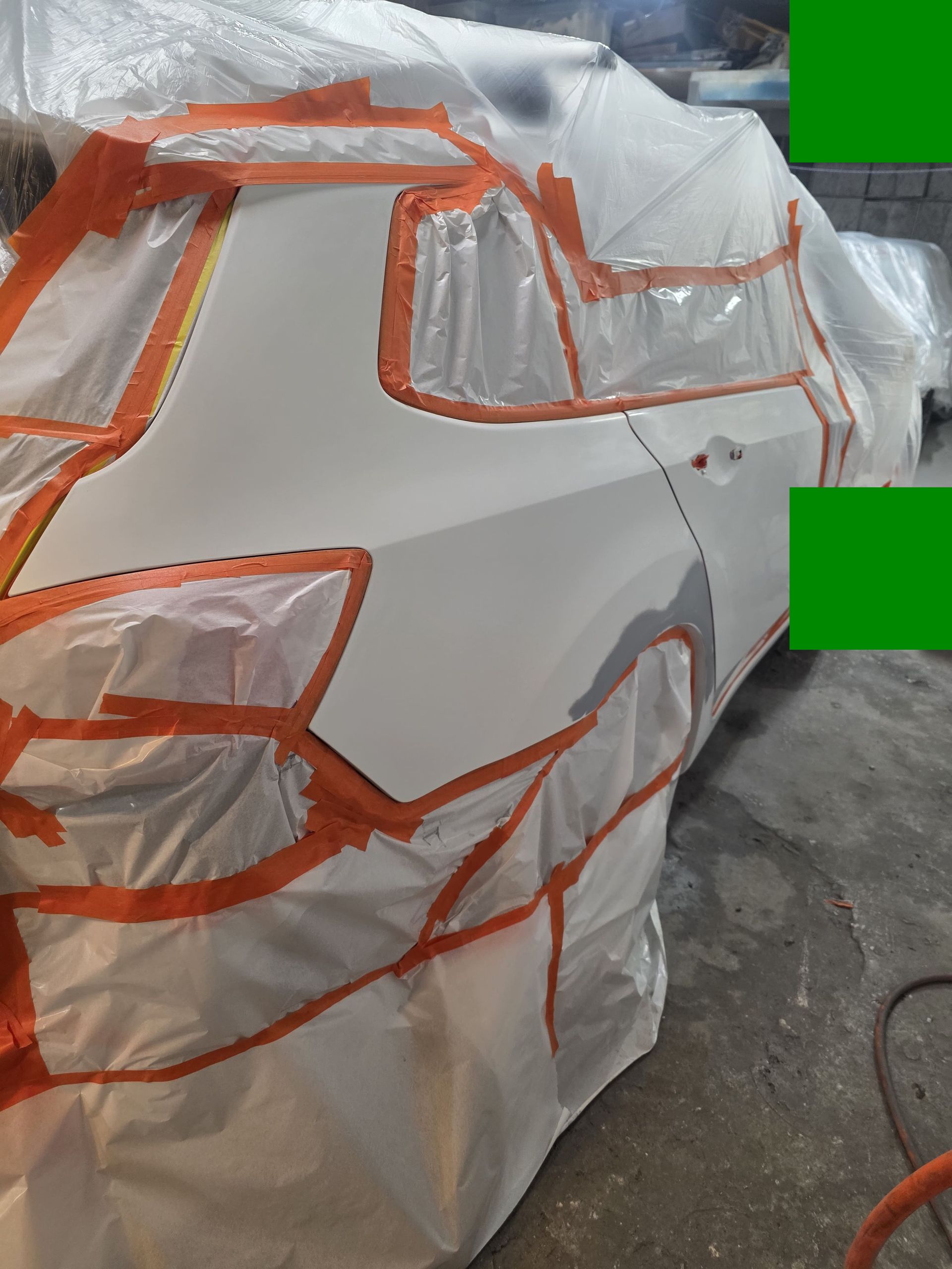 White car body covered in orange tape, likely for repair or masking in a workshop