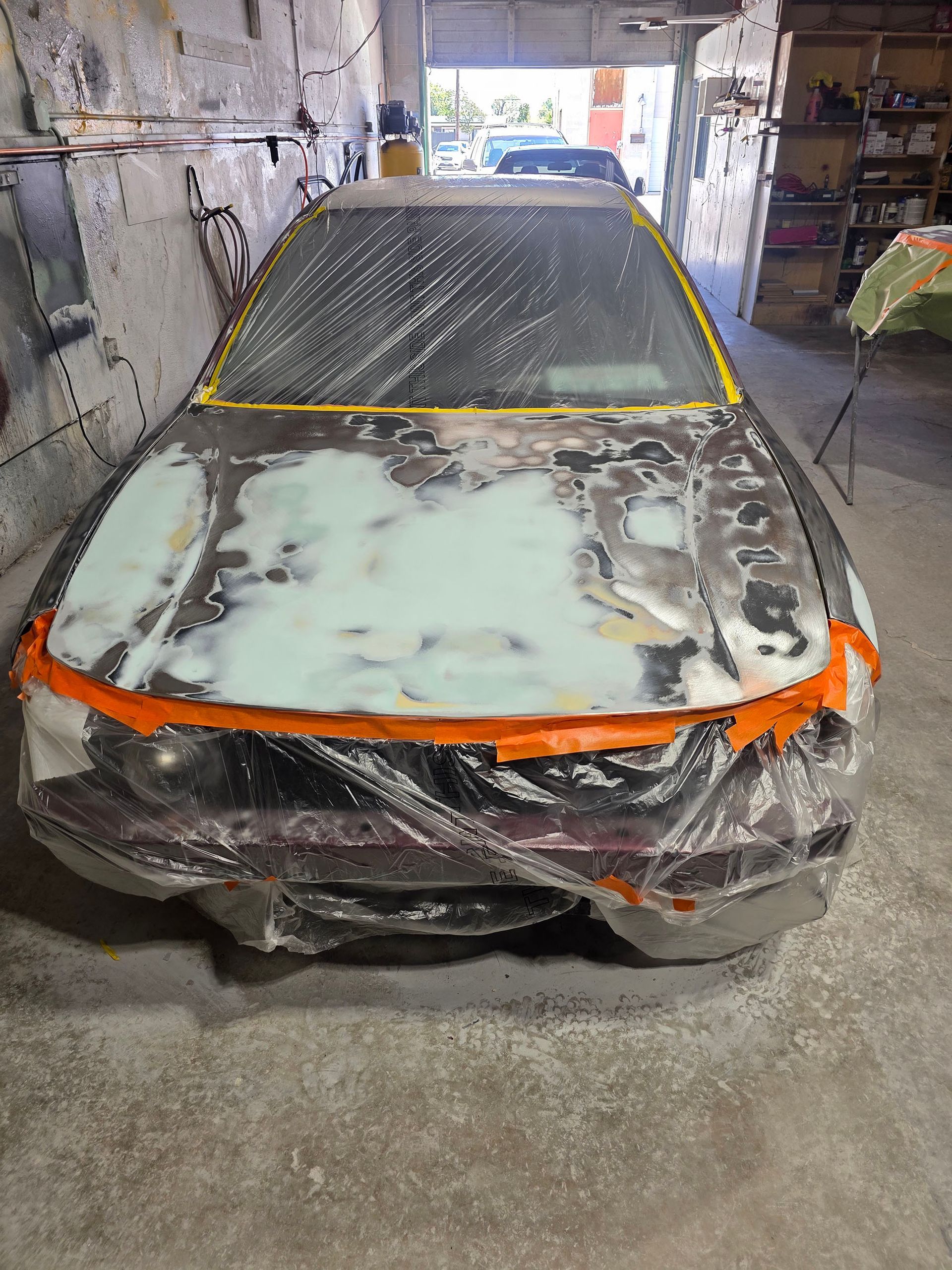 Car in auto body shop with front end covered in primer and masking tape, ready for paint
