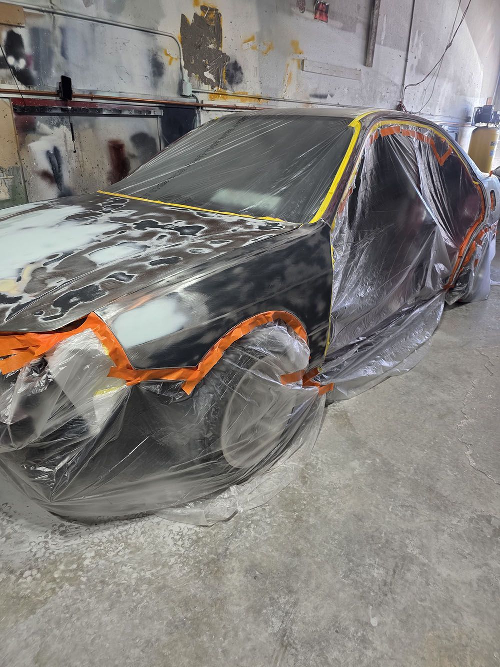 Car under repair, wrapped in plastic with orange and yellow masking tape in an auto body shop